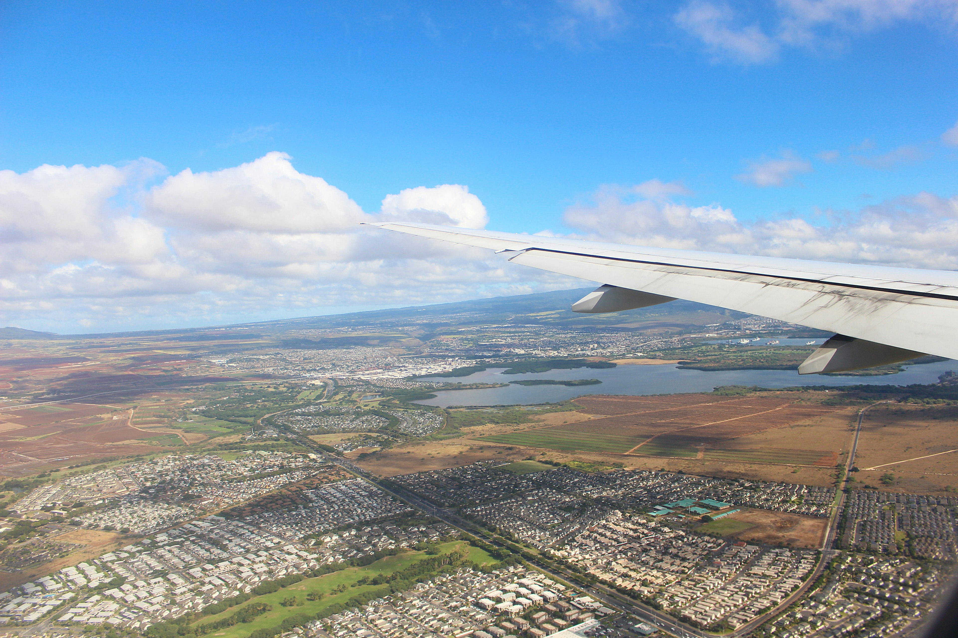 飛行機の翼から見た風景、青い空と雲、広がる都市と土地