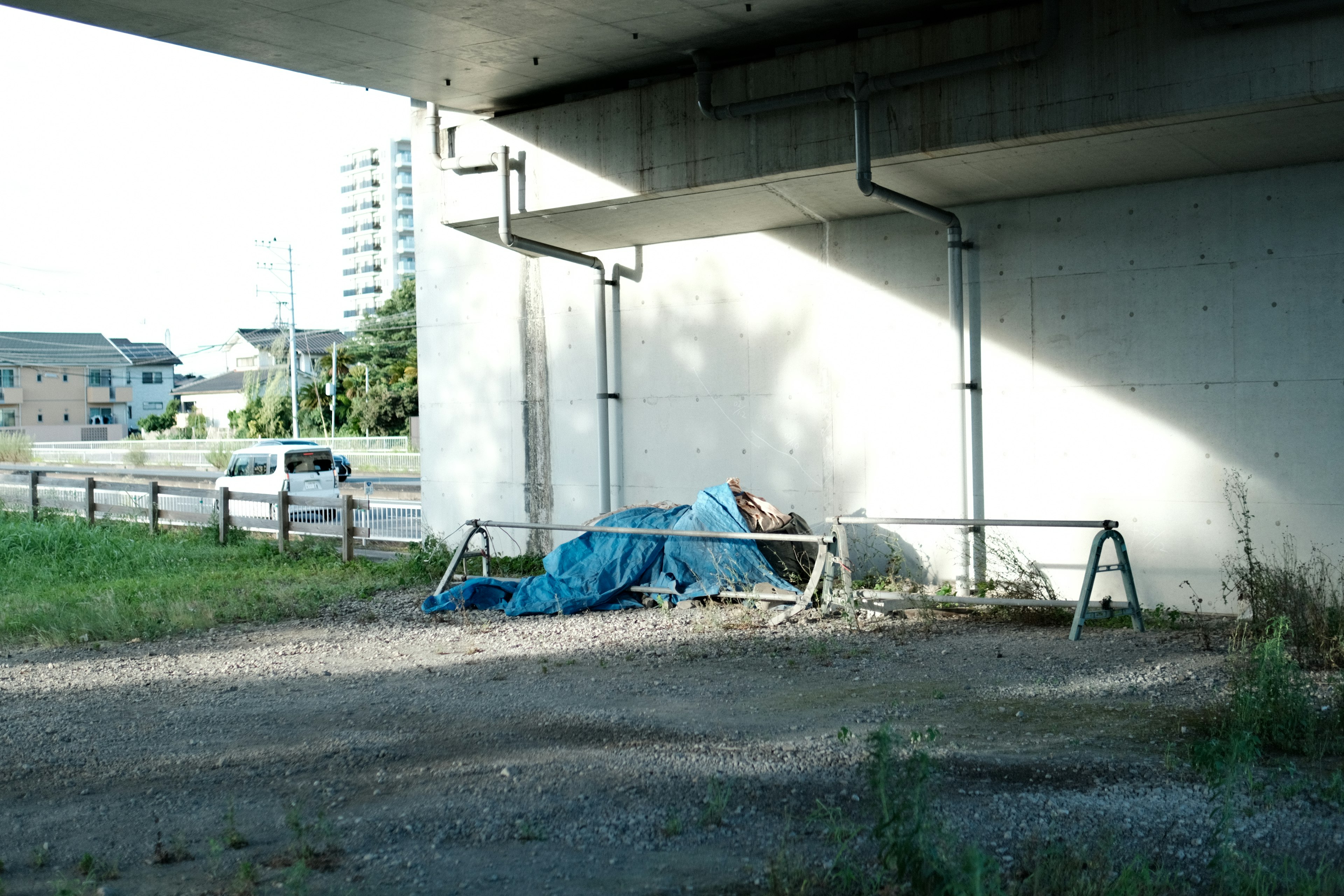 Object covered with a blue tarp under a bridge with surrounding landscape