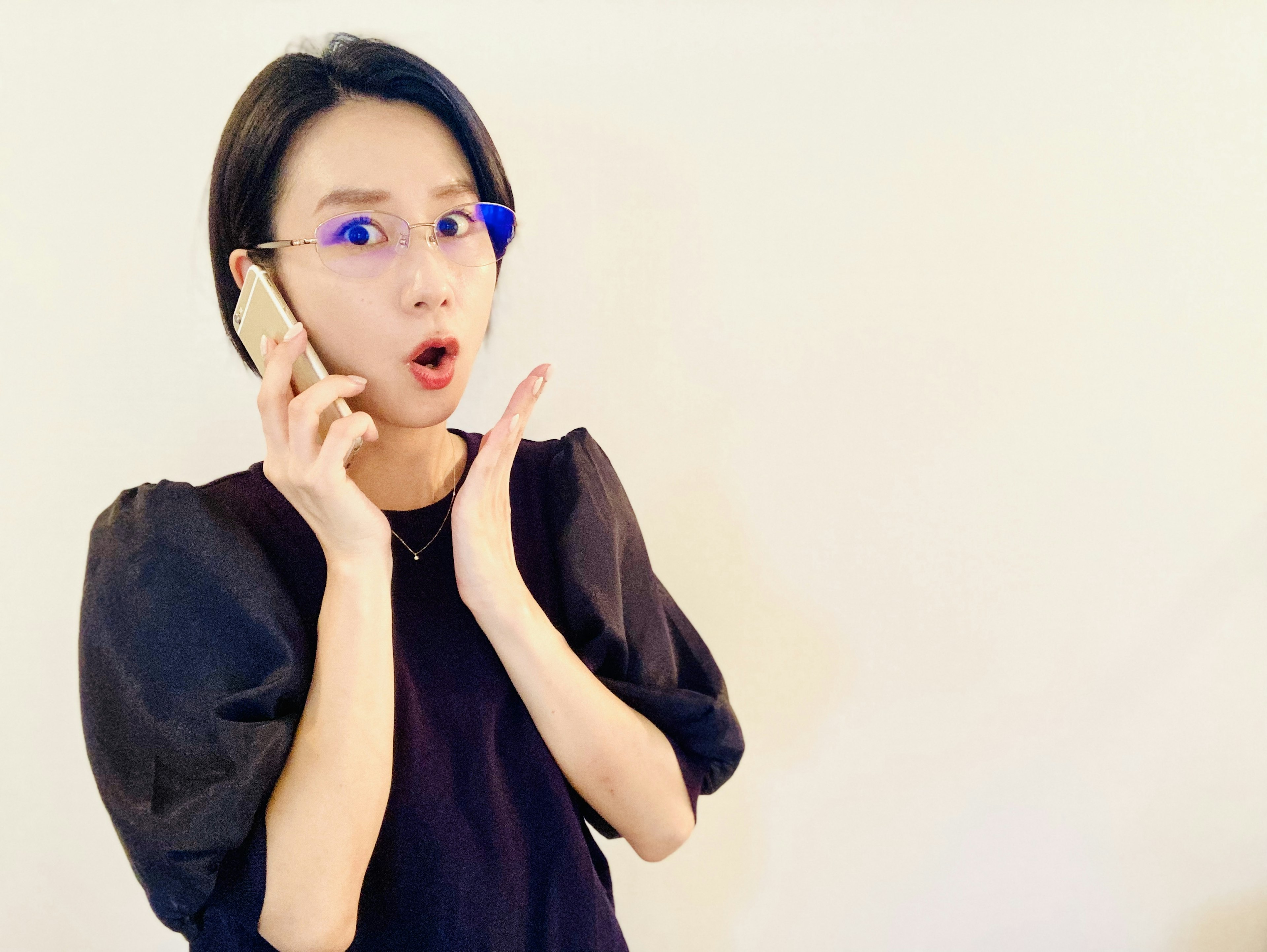 Surprised woman holding a phone wearing blue glasses against a simple background