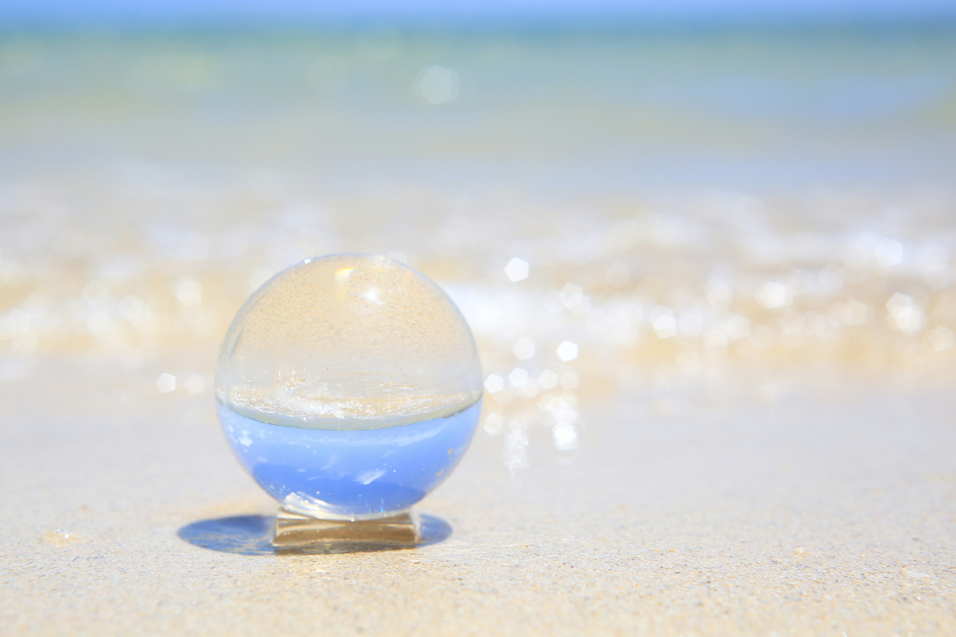 Sphère transparente placée sur une plage de sable avec des vagues océaniques en arrière-plan