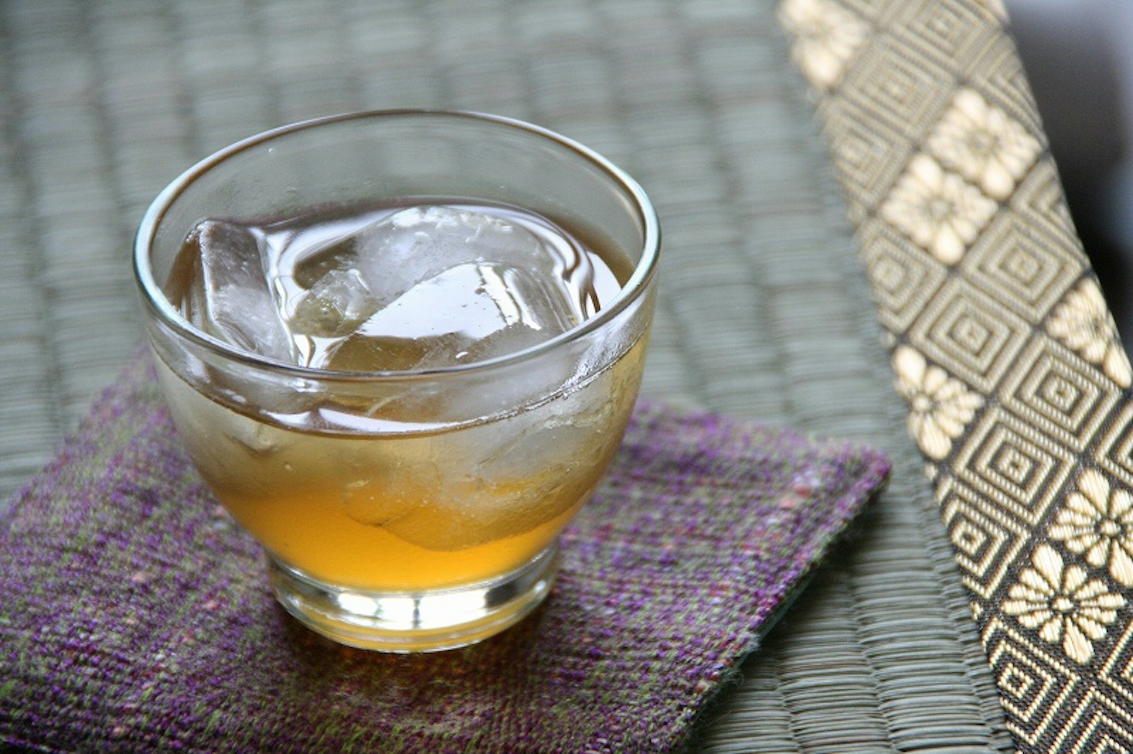 A glass of orange drink with ice on a textured table setting