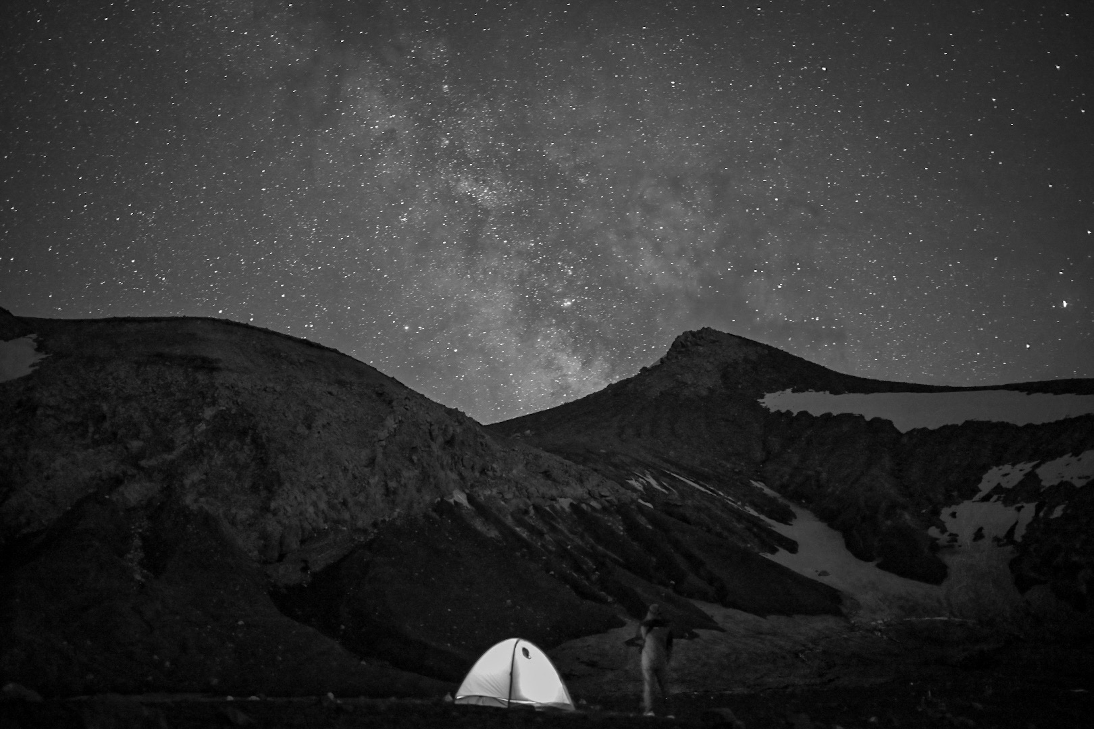 夜空に広がる星々と山々のシルエットが見えるキャンプテント