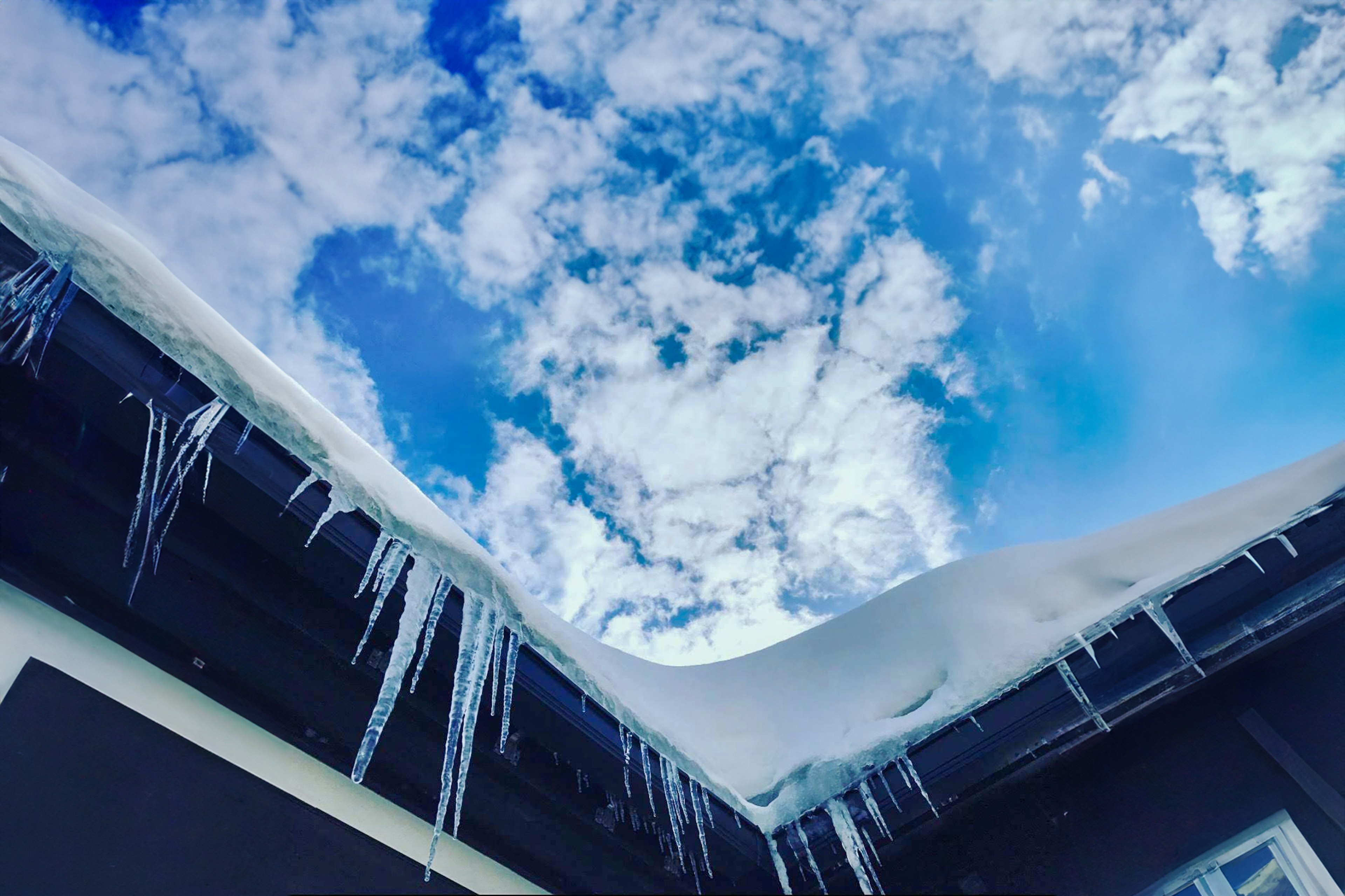 雪と氷柱がある屋根の下から見上げた青空と雲