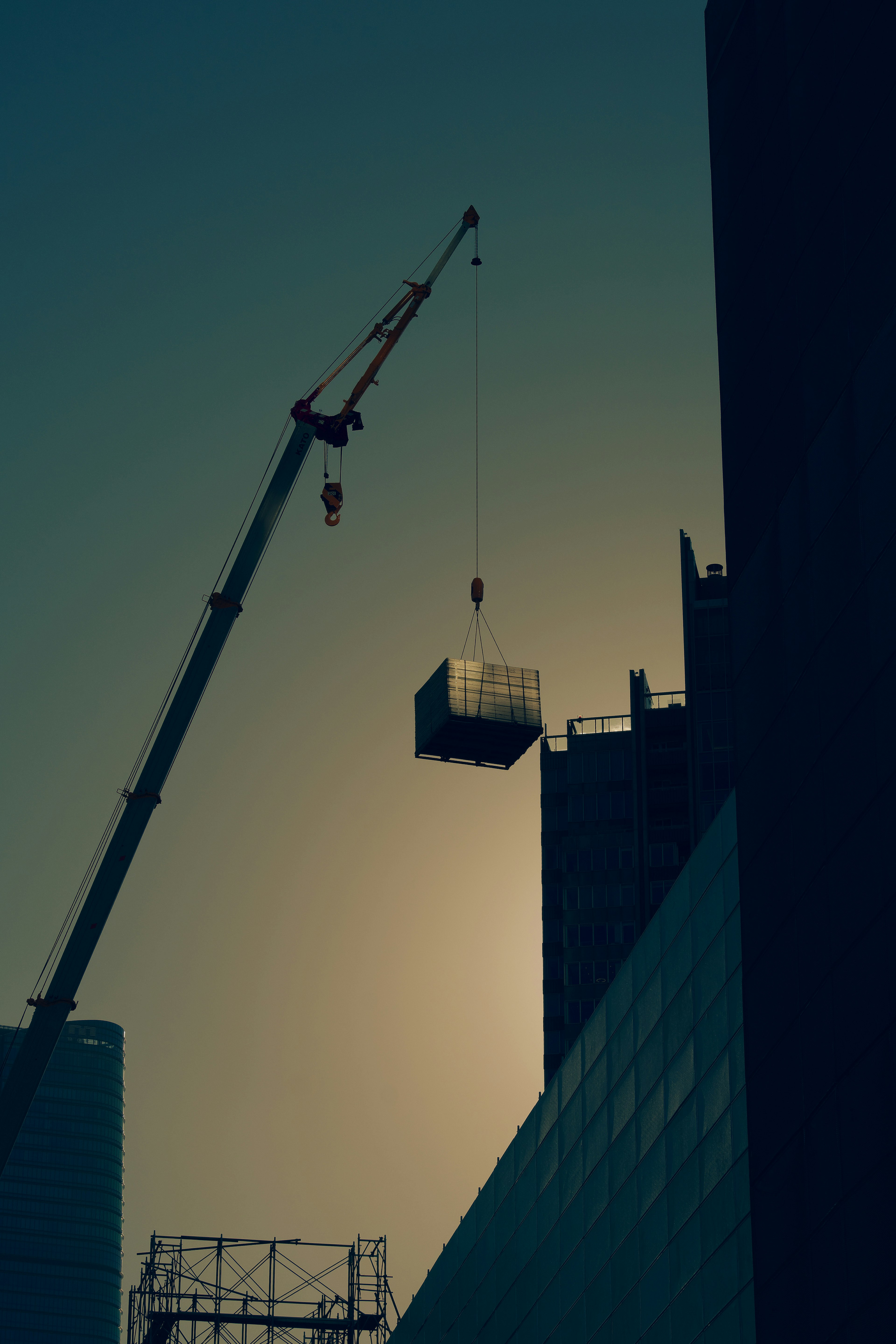 Silhouette di una gru che solleva un carico sopra un edificio al tramonto