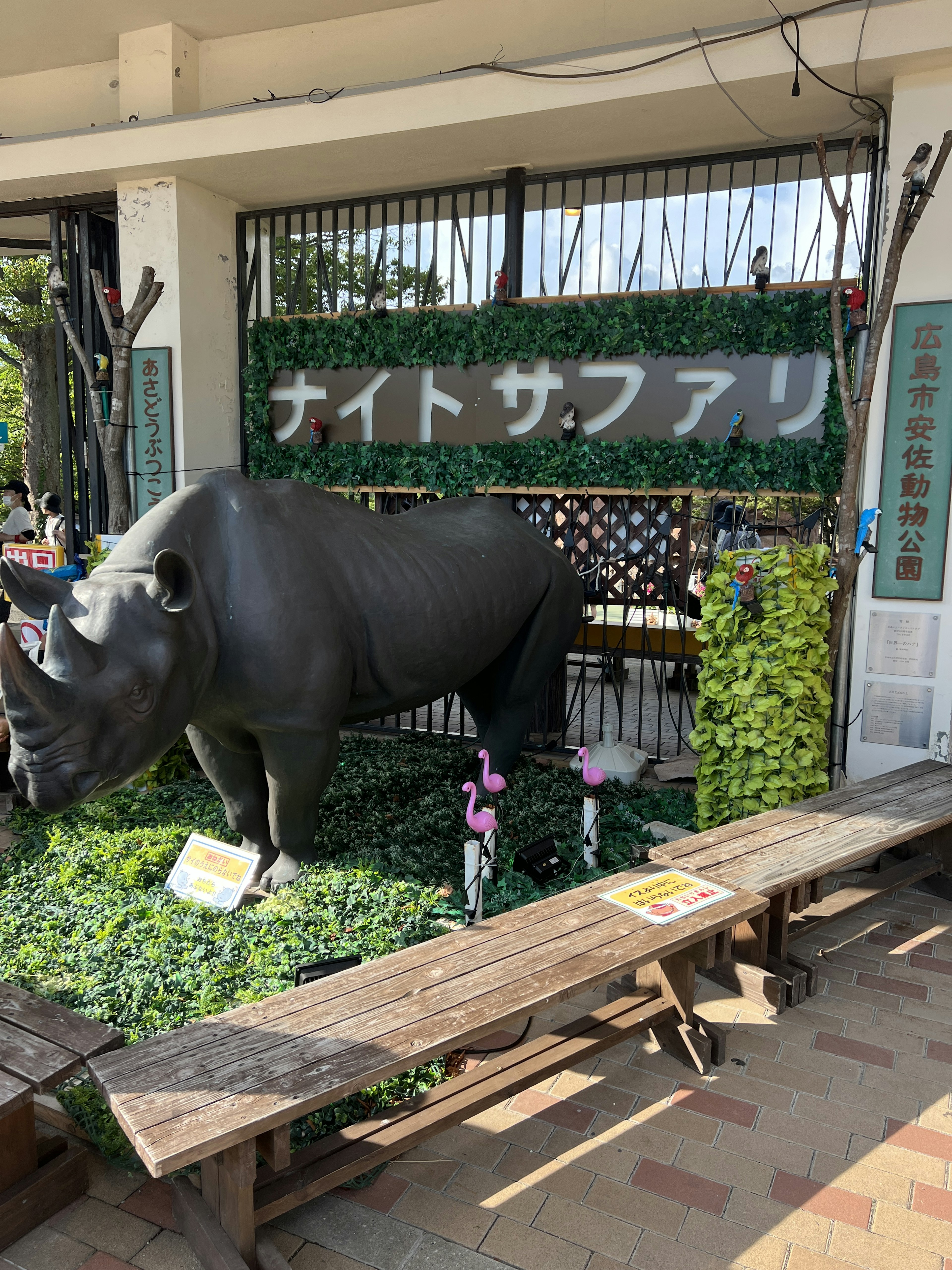 夜間野生動物園標誌前的黑犀牛雕像，周圍環繞著綠色植物