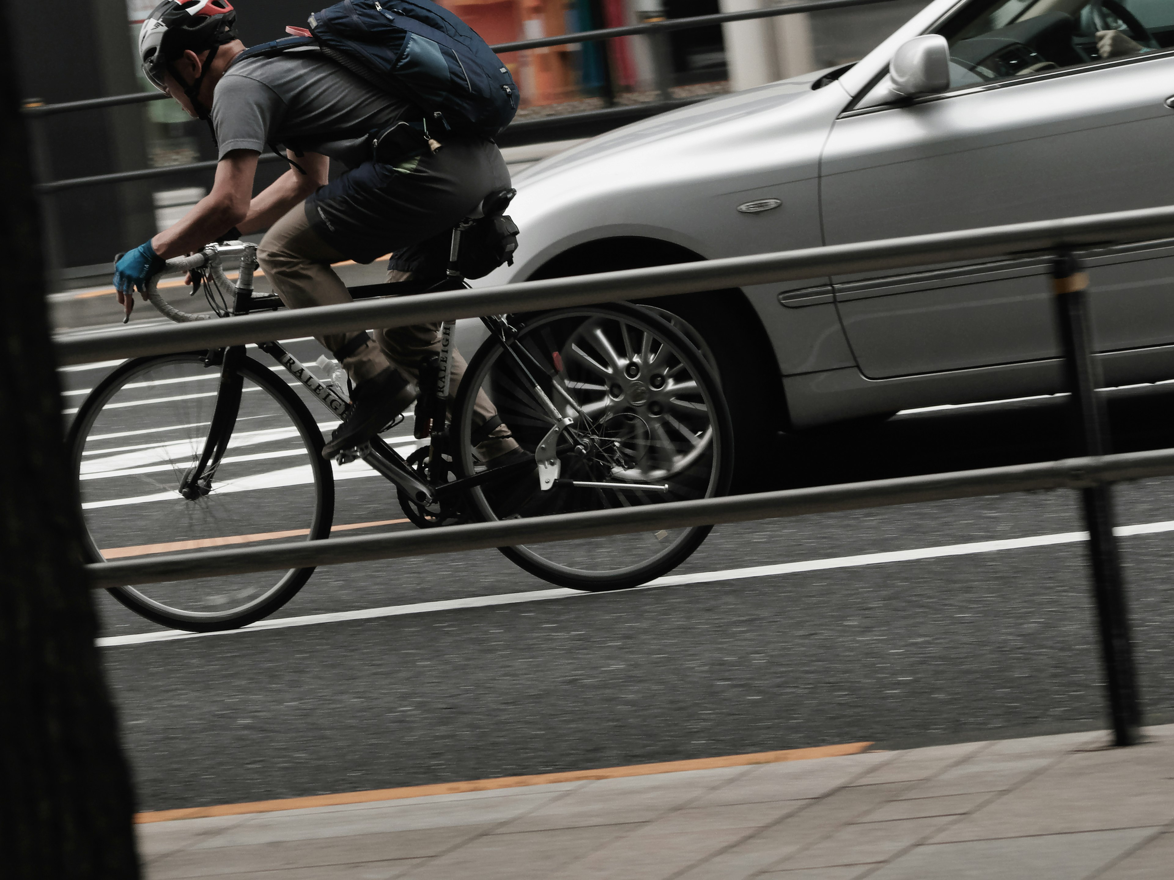 自転車に乗る男性と銀色の車が通る都市の風景