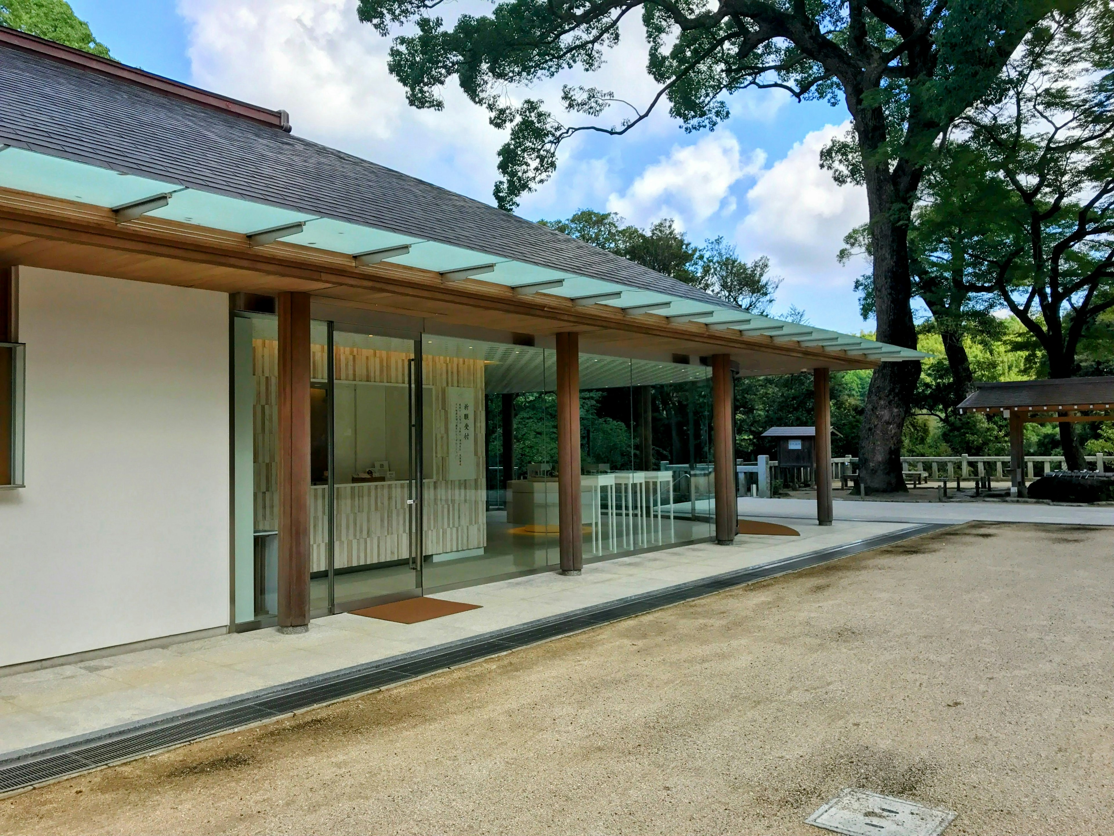 Modern architectural exterior featuring wooden pillars and glass walls with blue sky and green trees in the background