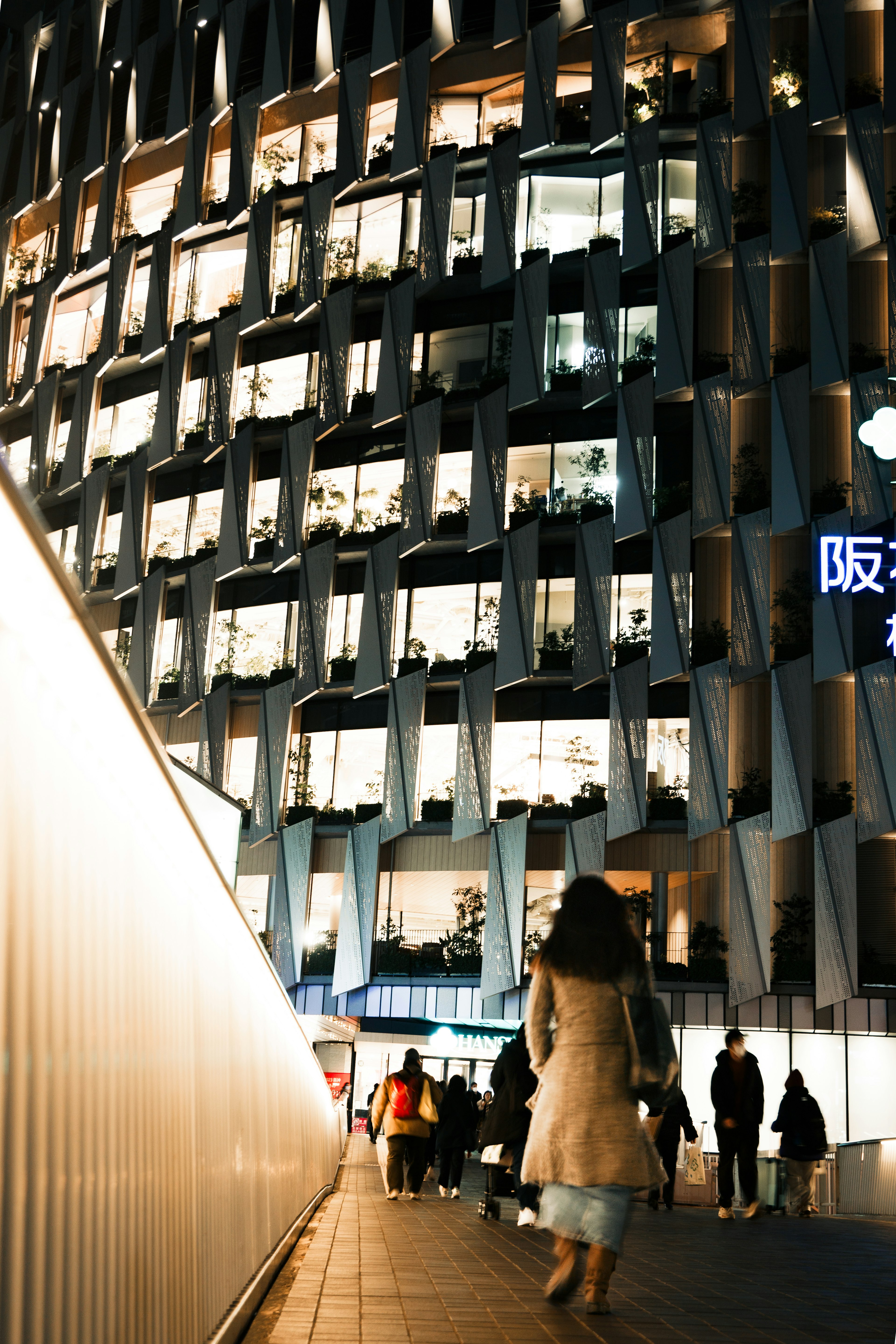 夜の都市景観で人々が行き交う中、現代的な建物のファサードが照明で輝いている