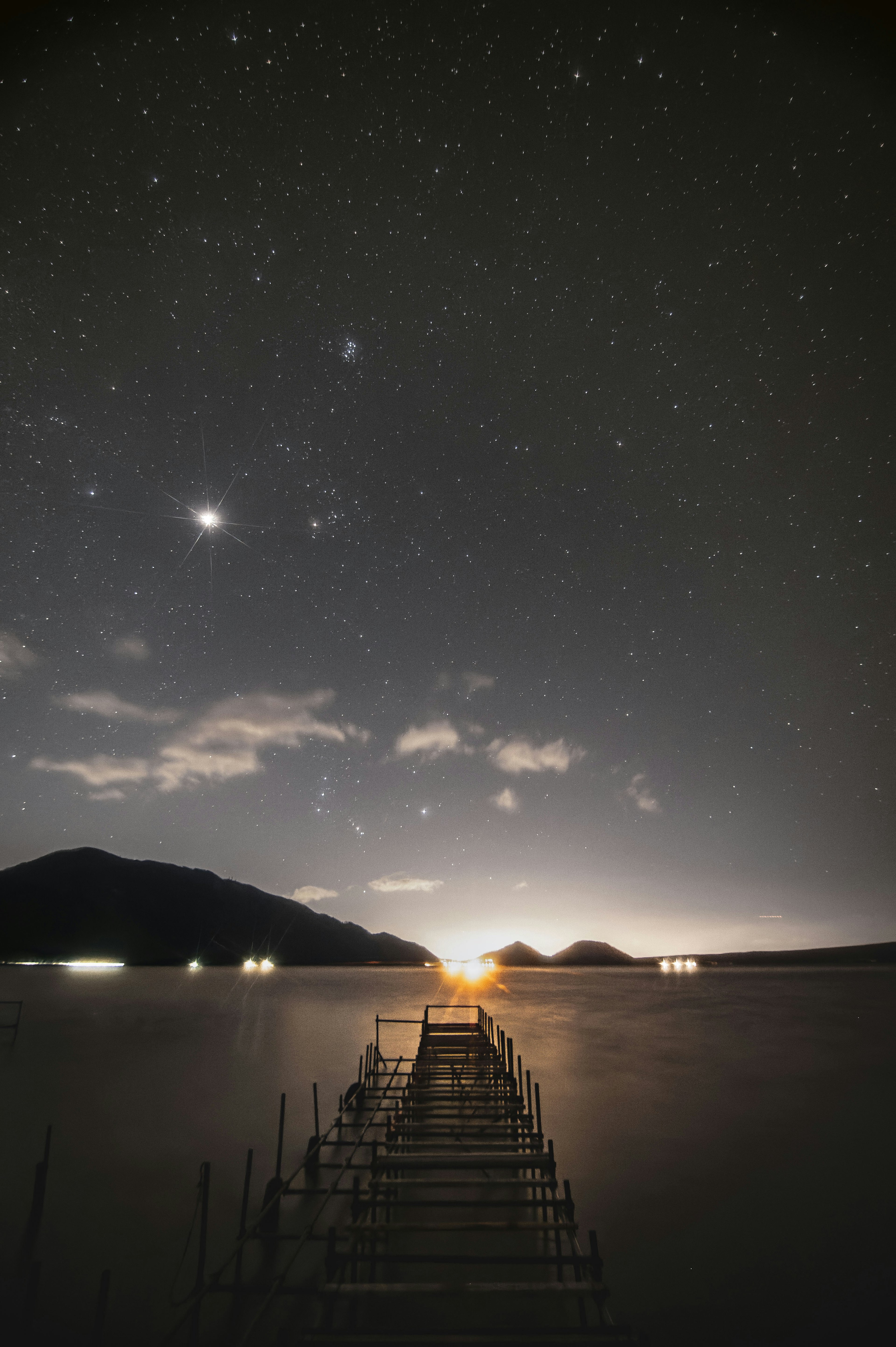 Pier extending into a lake under a starry sky with distant mountains