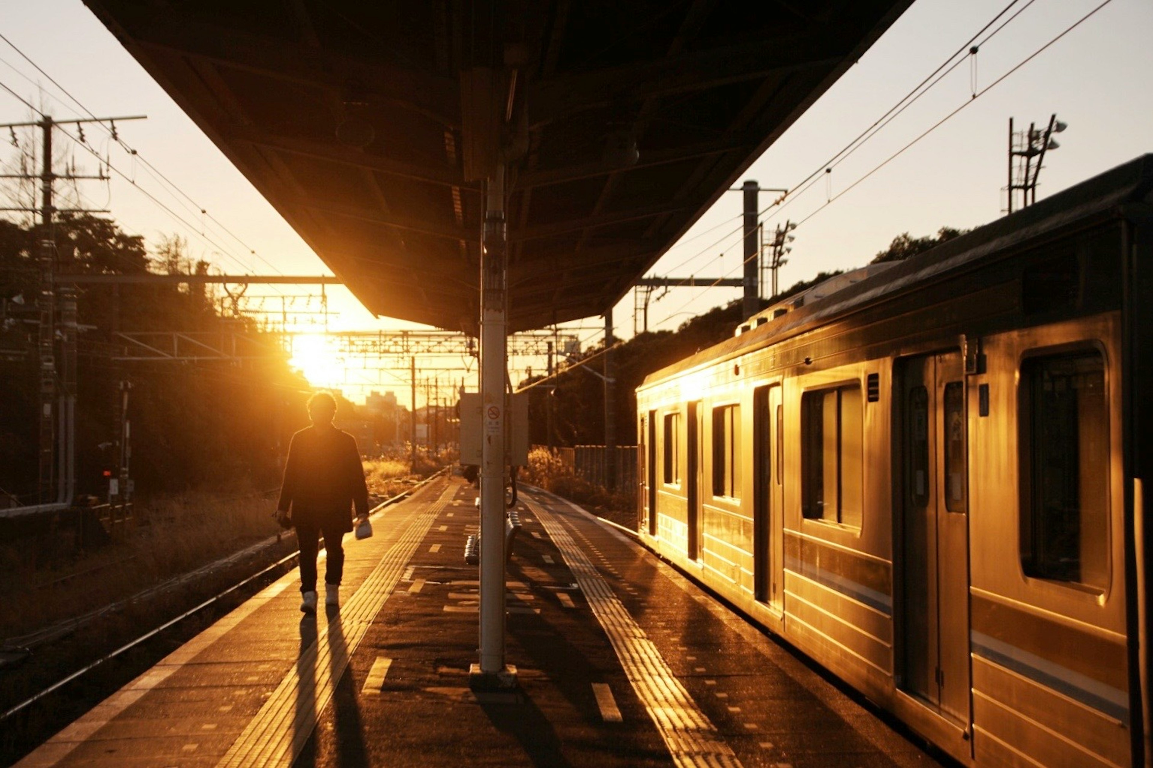 夕日が差し込む駅のプラットフォームで歩く人影と列車