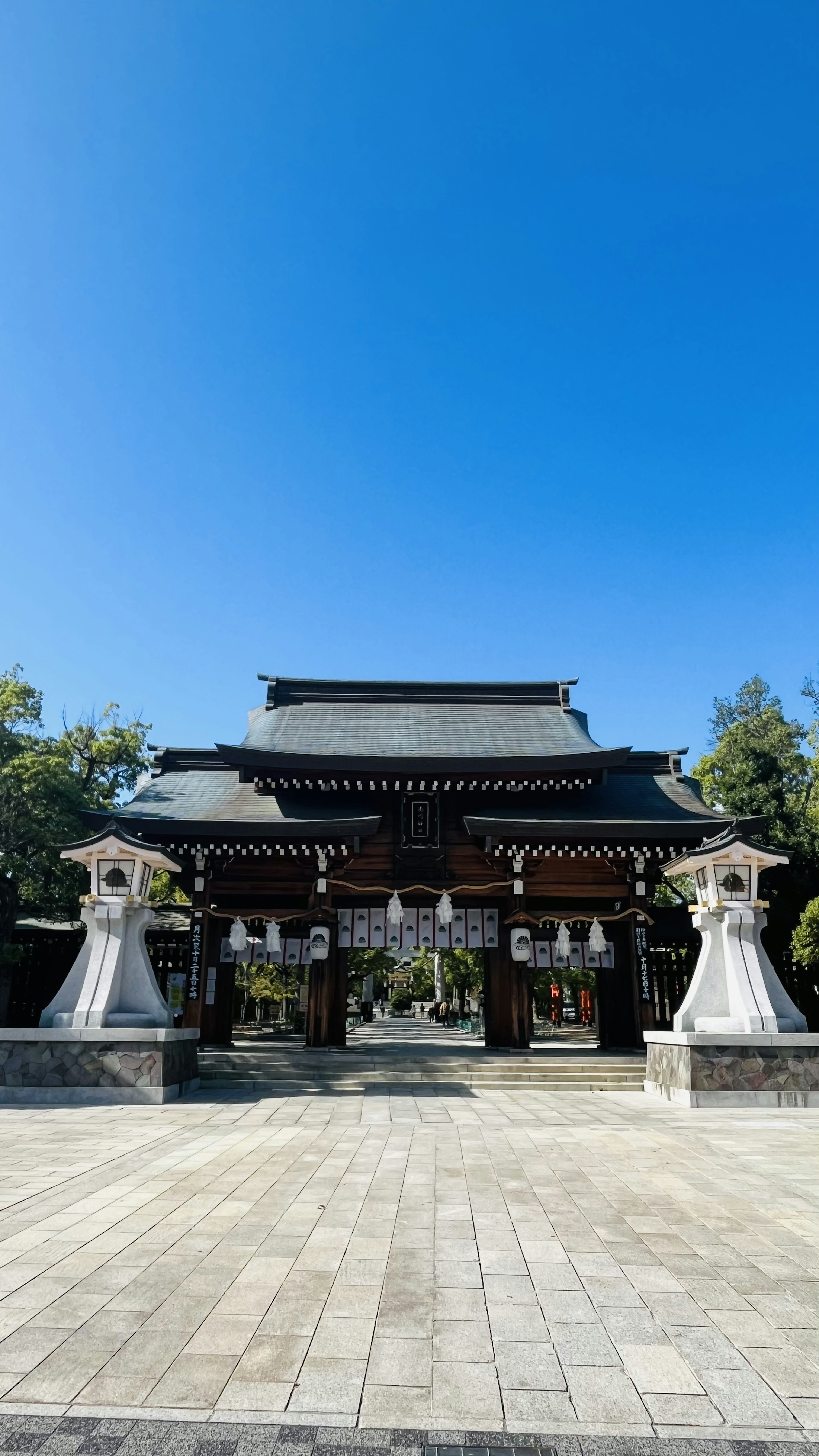 藍天之下的傳統神社入口，兩側有守護神像