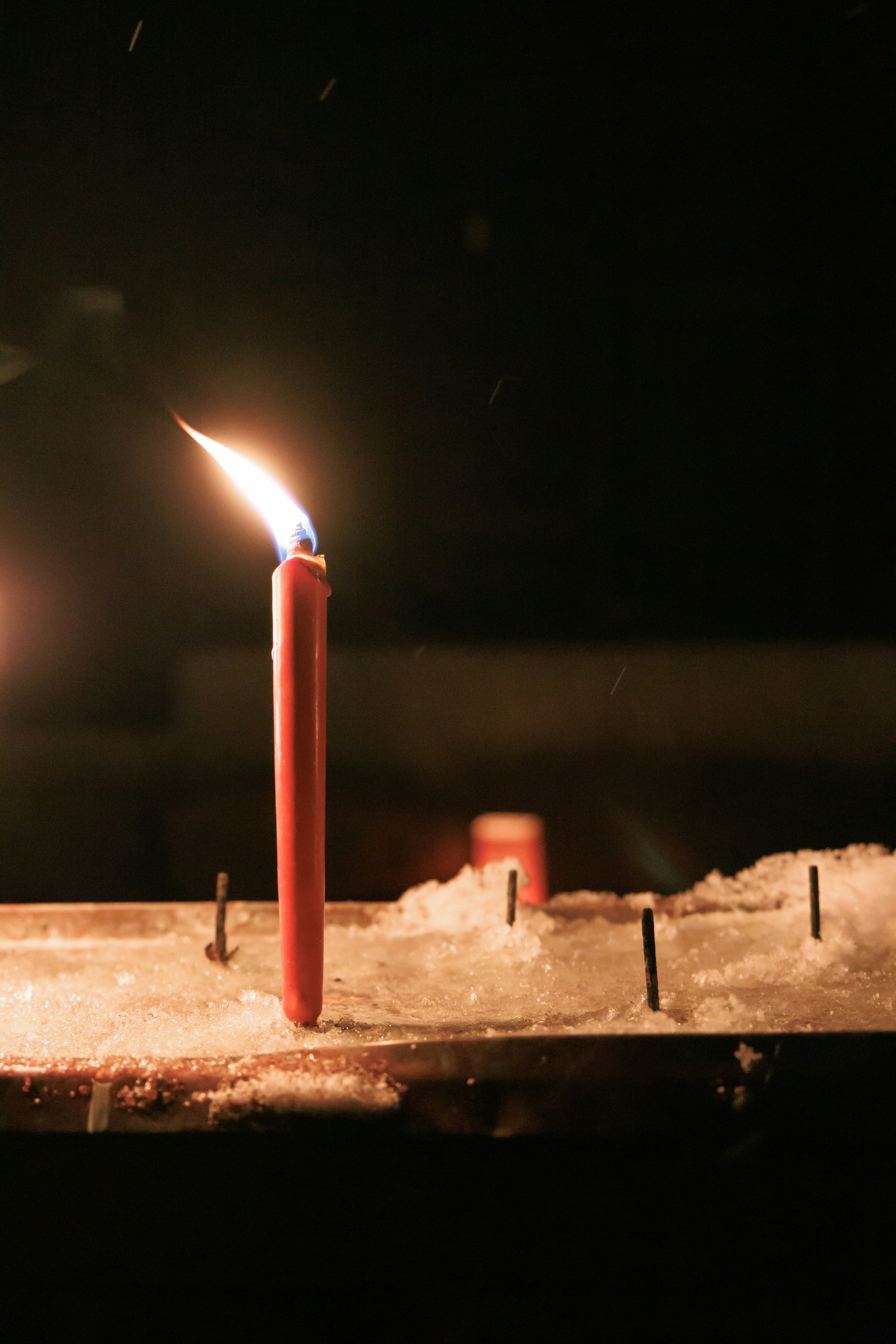 Sebuah lilin merah menyala di latar belakang gelap dengan salju