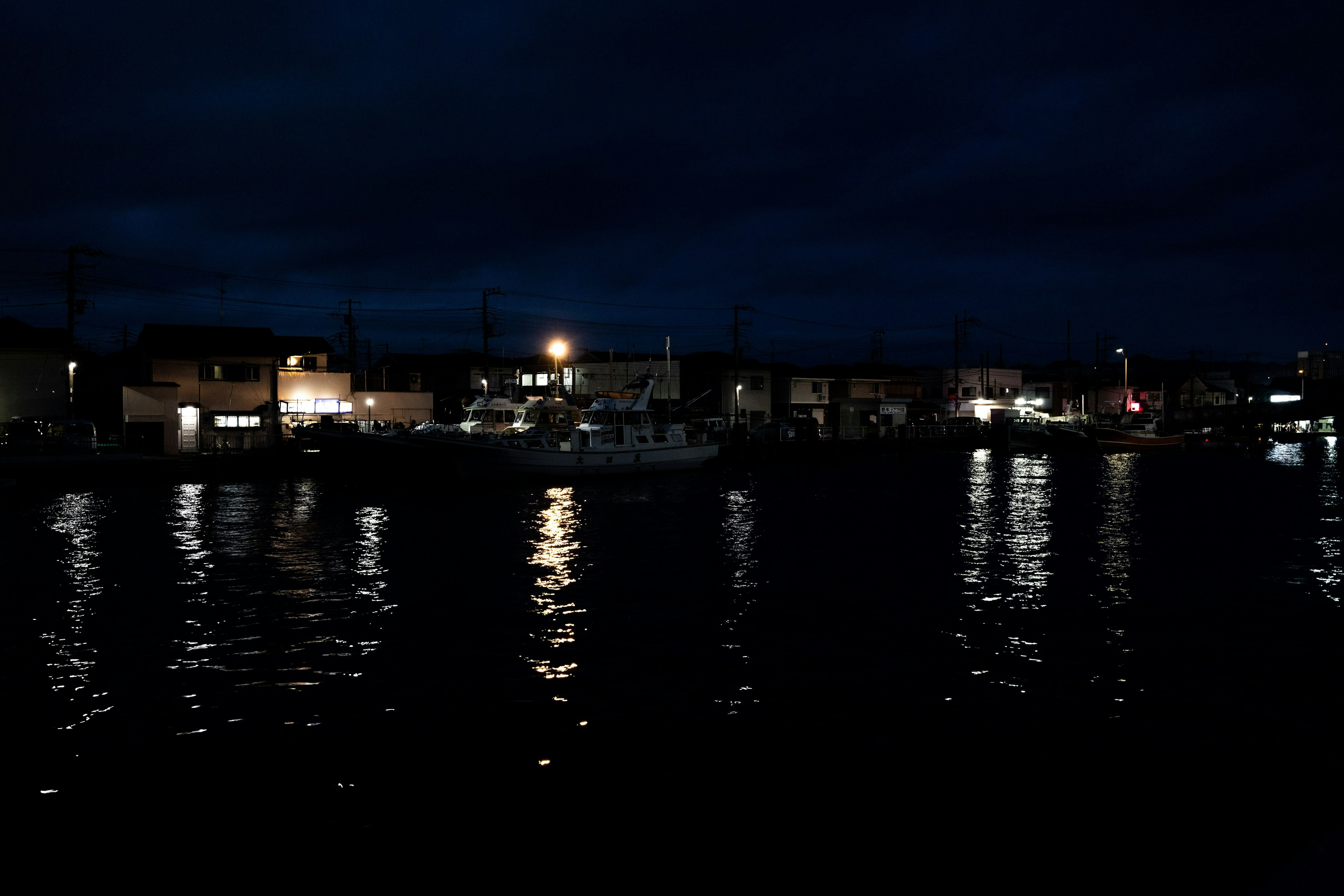 Scène de port nocturne avec des lumières se reflétant sur l'eau et des nuages sombres