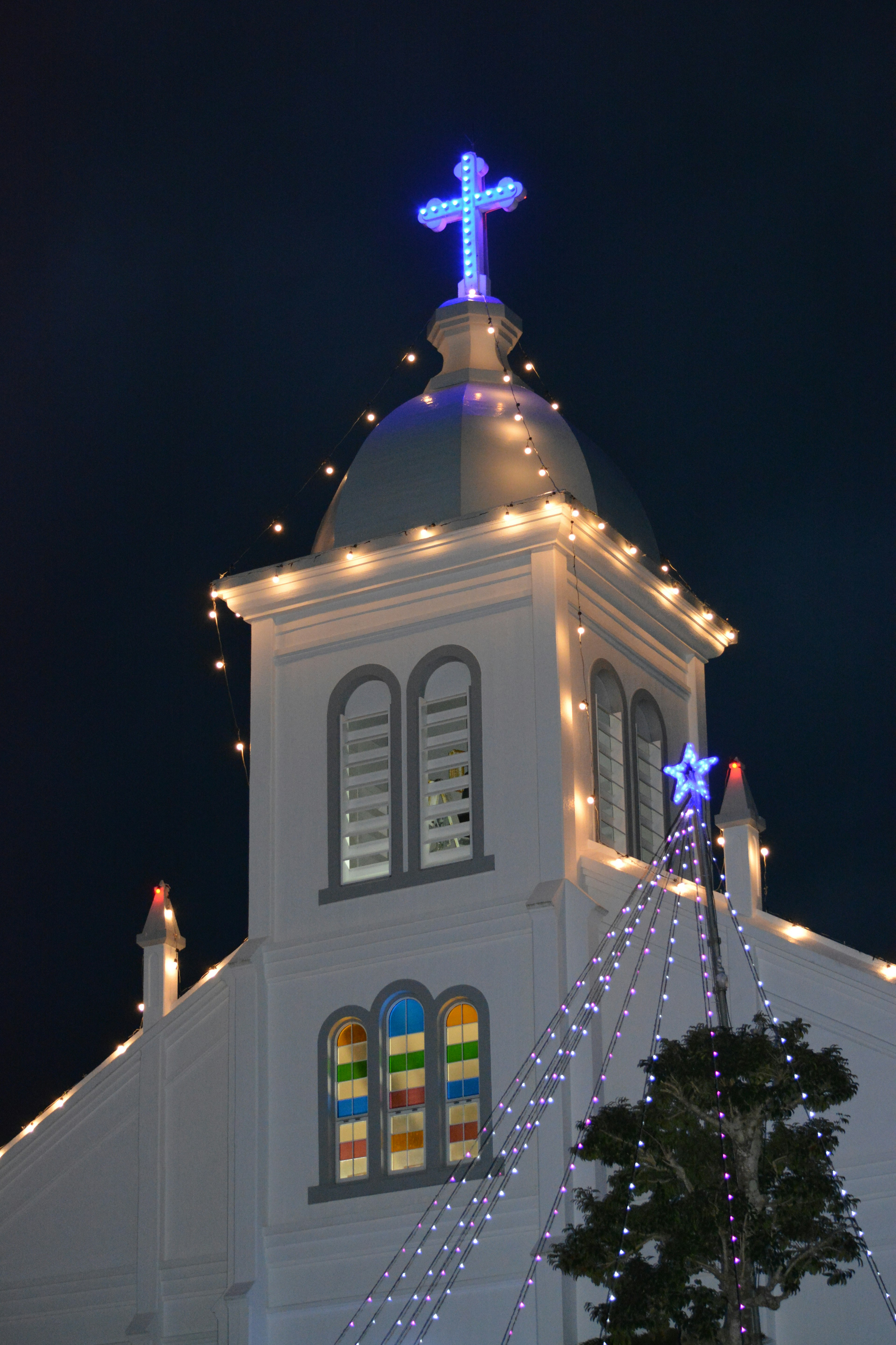 Toit d'église décoré de lumières et d'une croix lumineuse la nuit