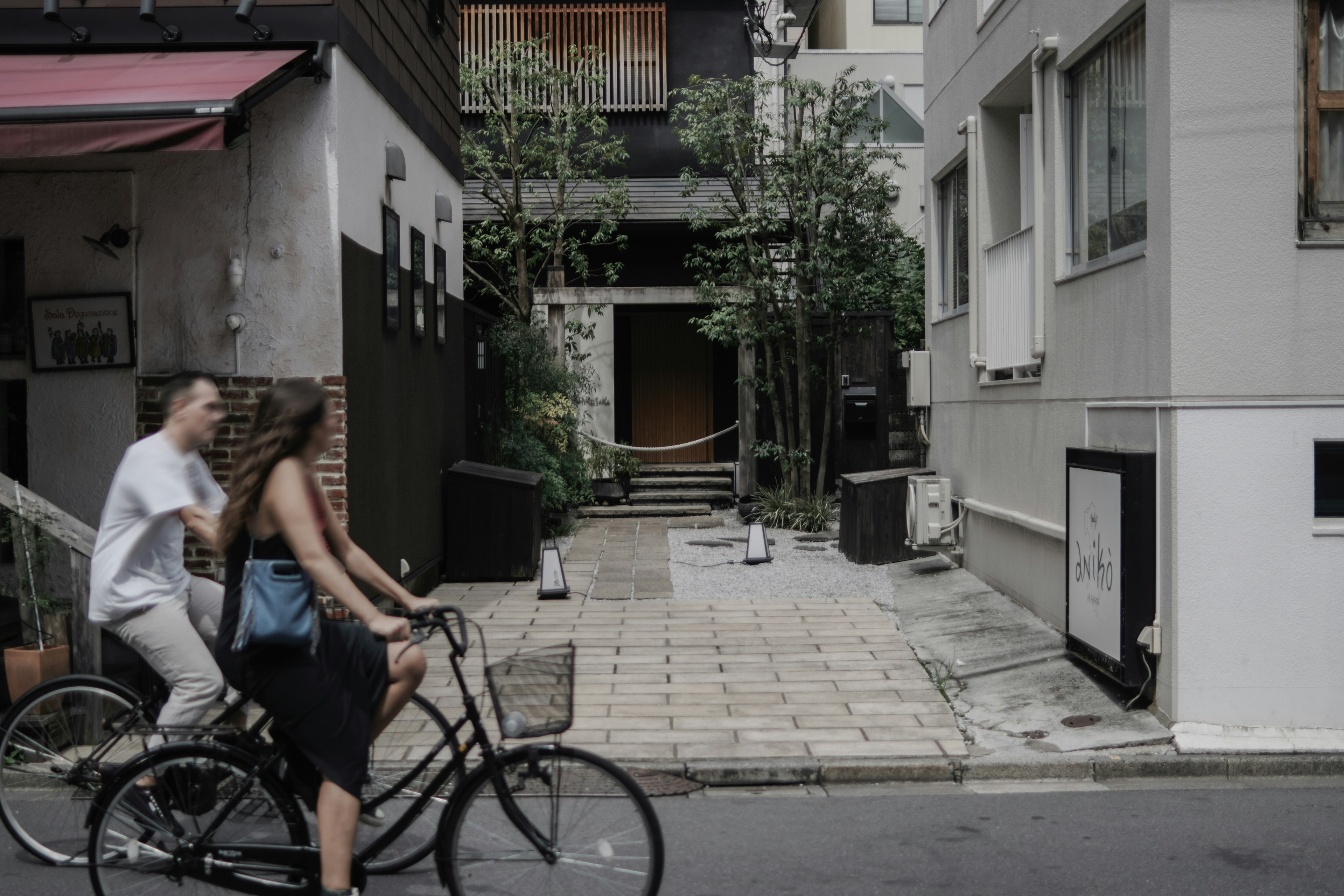 Una coppia in bicicletta su una strada stretta con vegetazione e edifici sullo sfondo