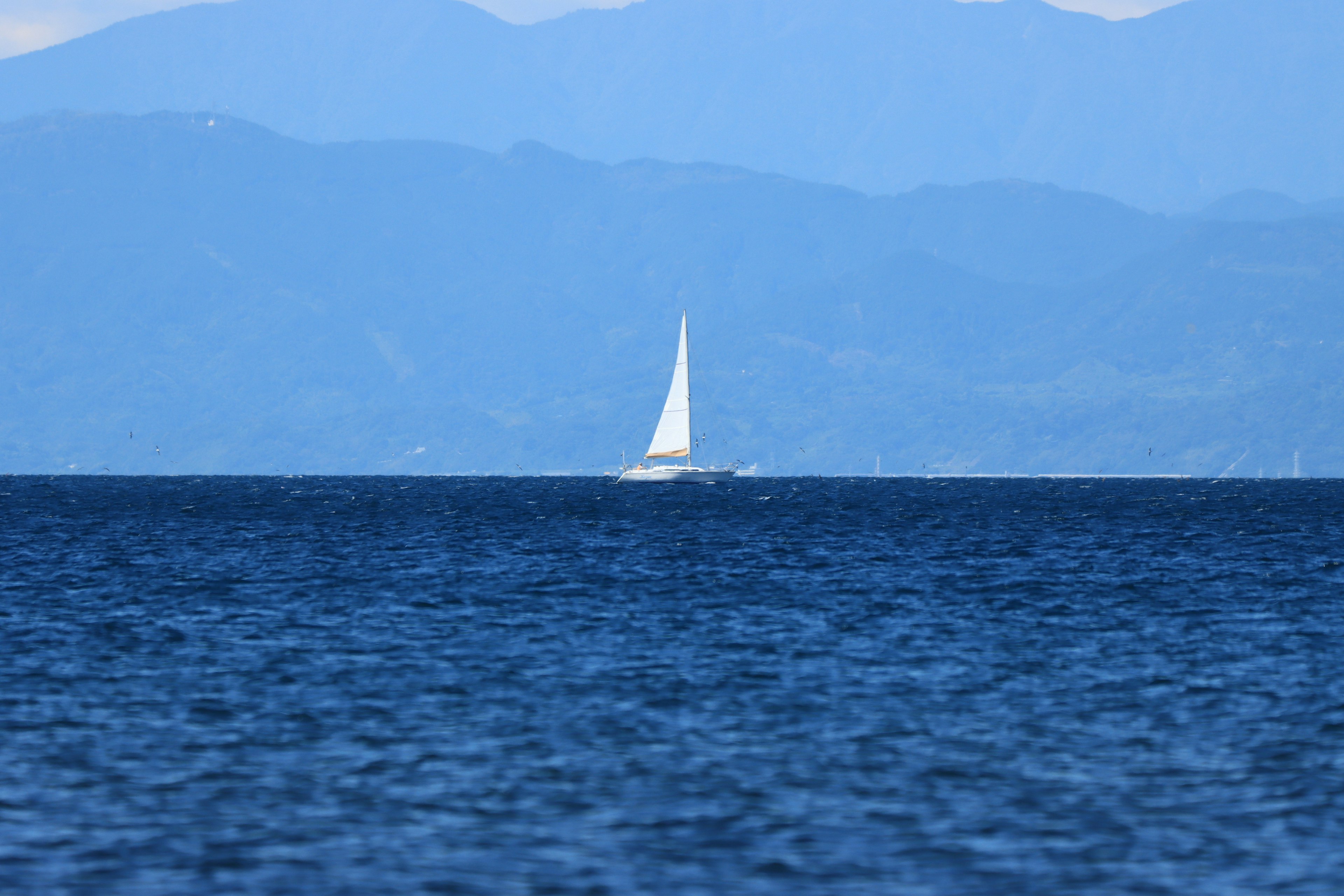 Perahu layar putih di atas air biru dengan latar belakang pegunungan