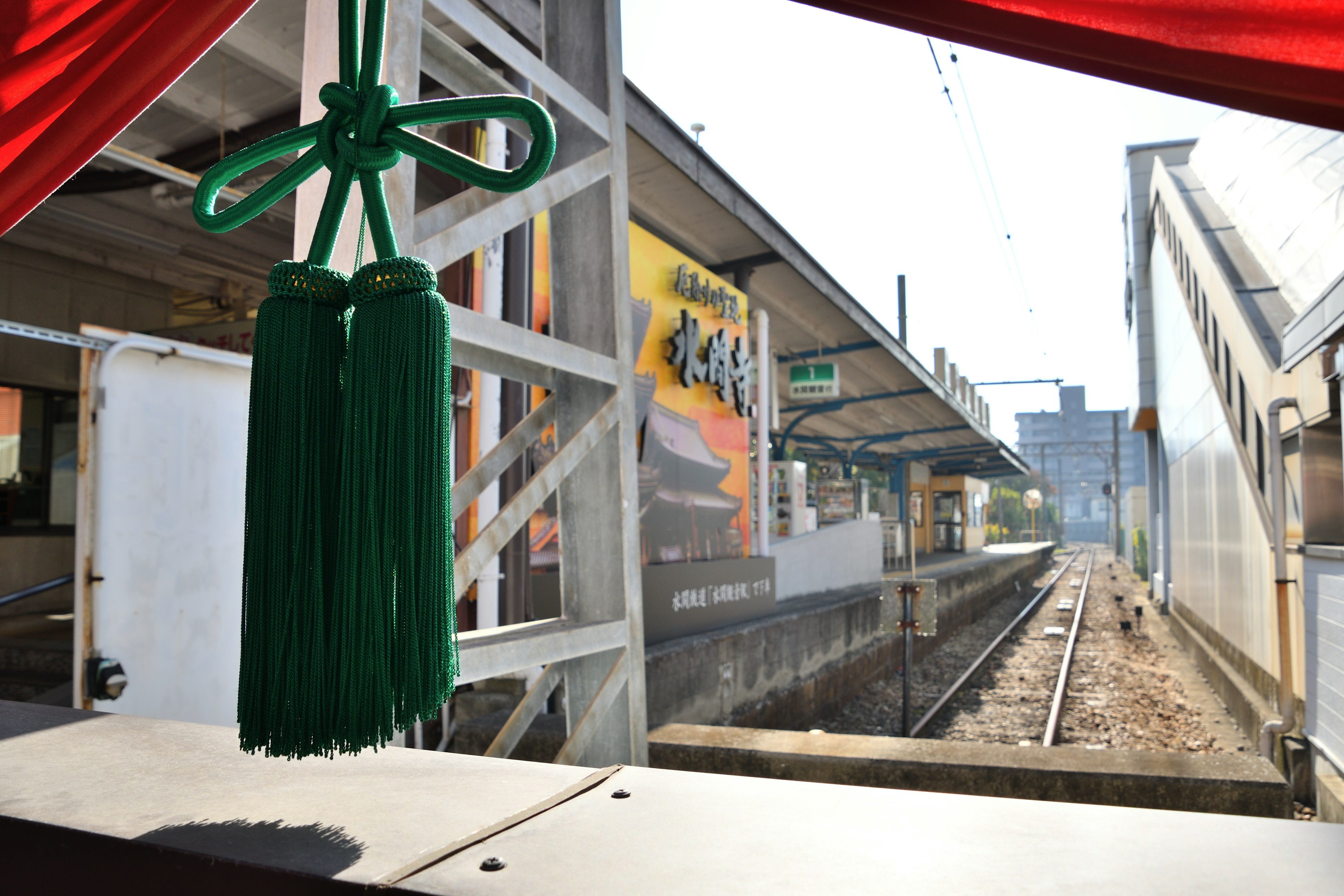 駅のプラットフォームが見える窓からの景色 緑色の飾り紐が前景に見える