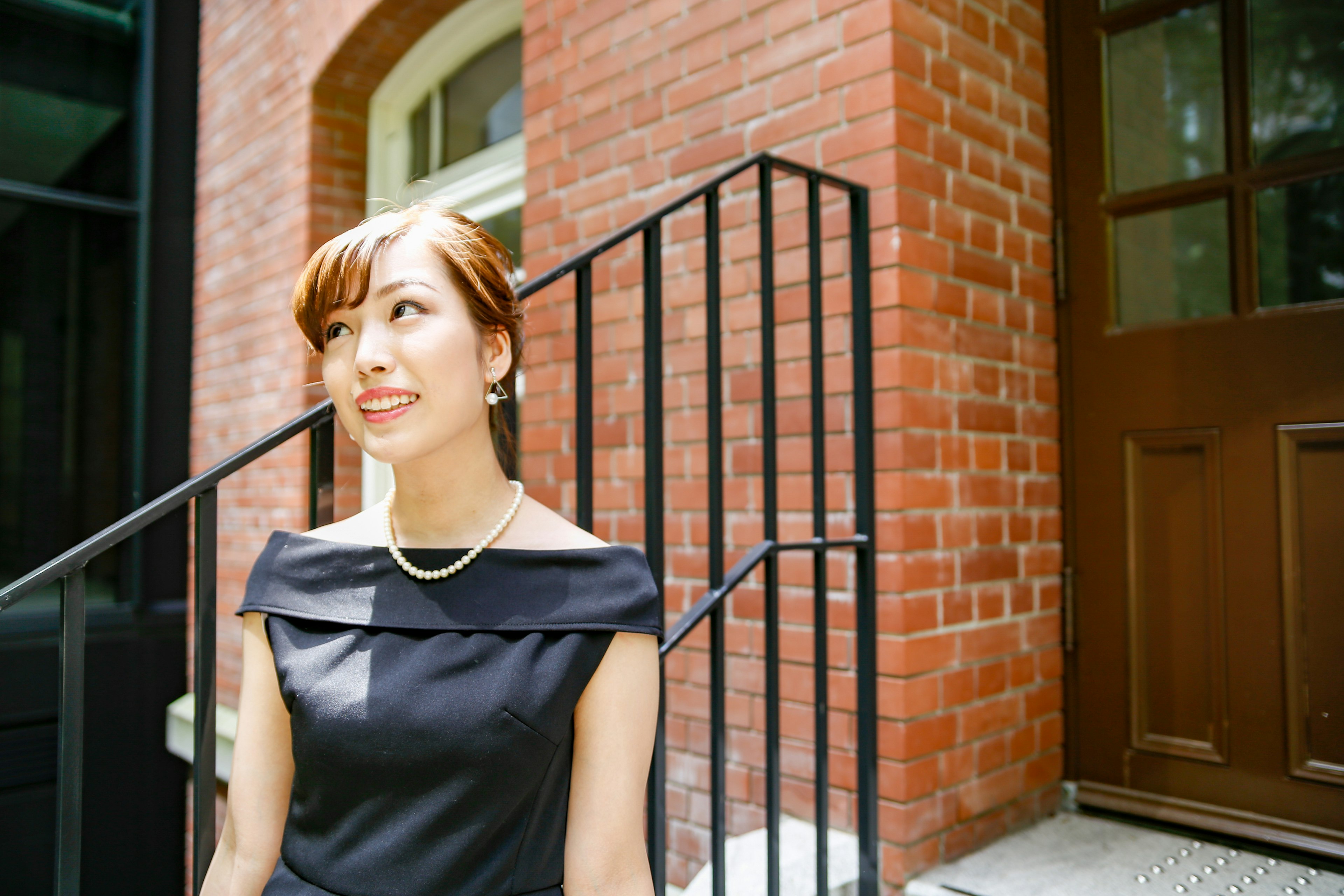 A woman in a black dress smiling in front of a brick building