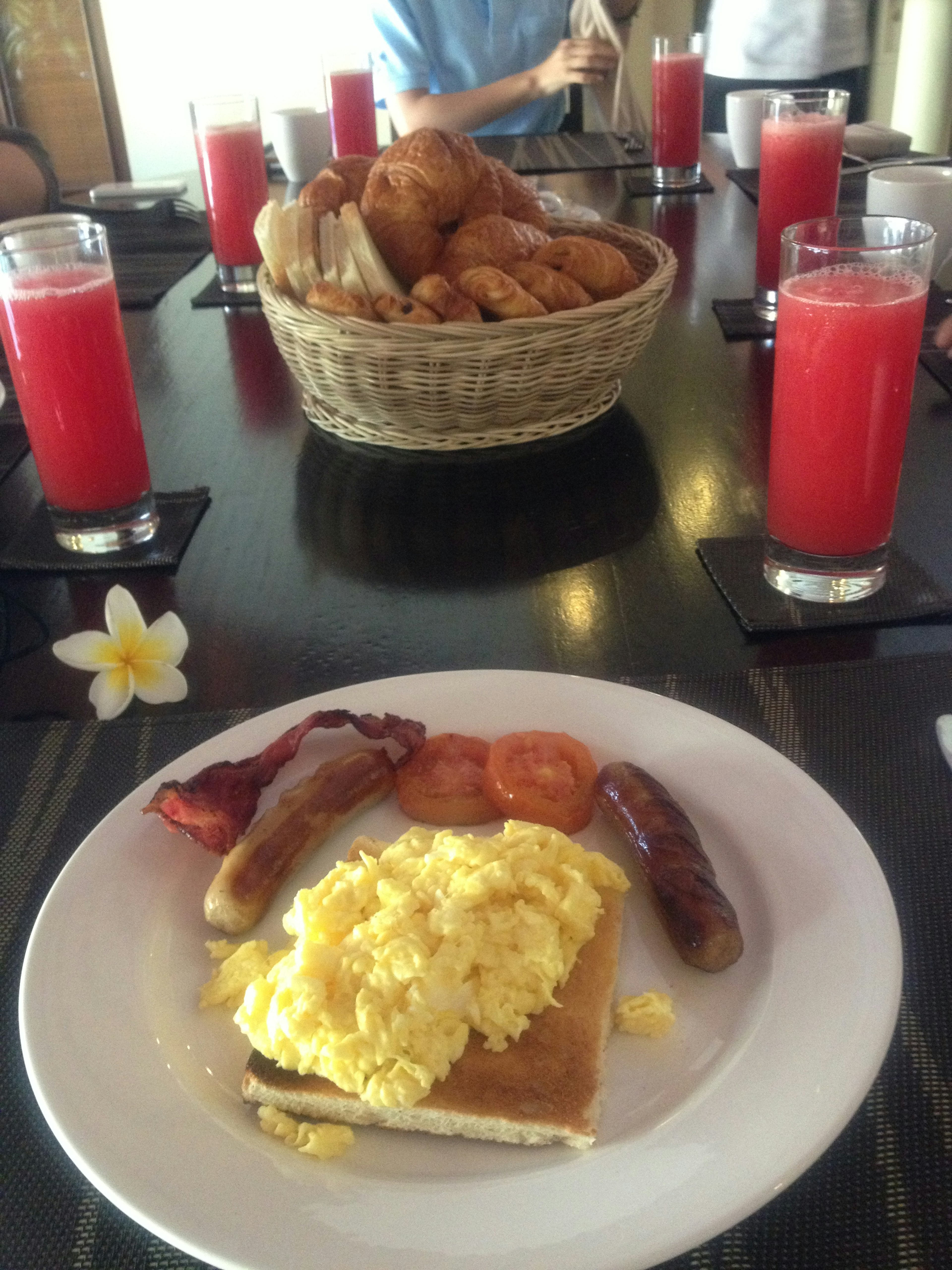 Une assiette de petit-déjeuner avec des œufs brouillés des saucisses et des tomates Un panier de pain et de pâtisseries en arrière-plan