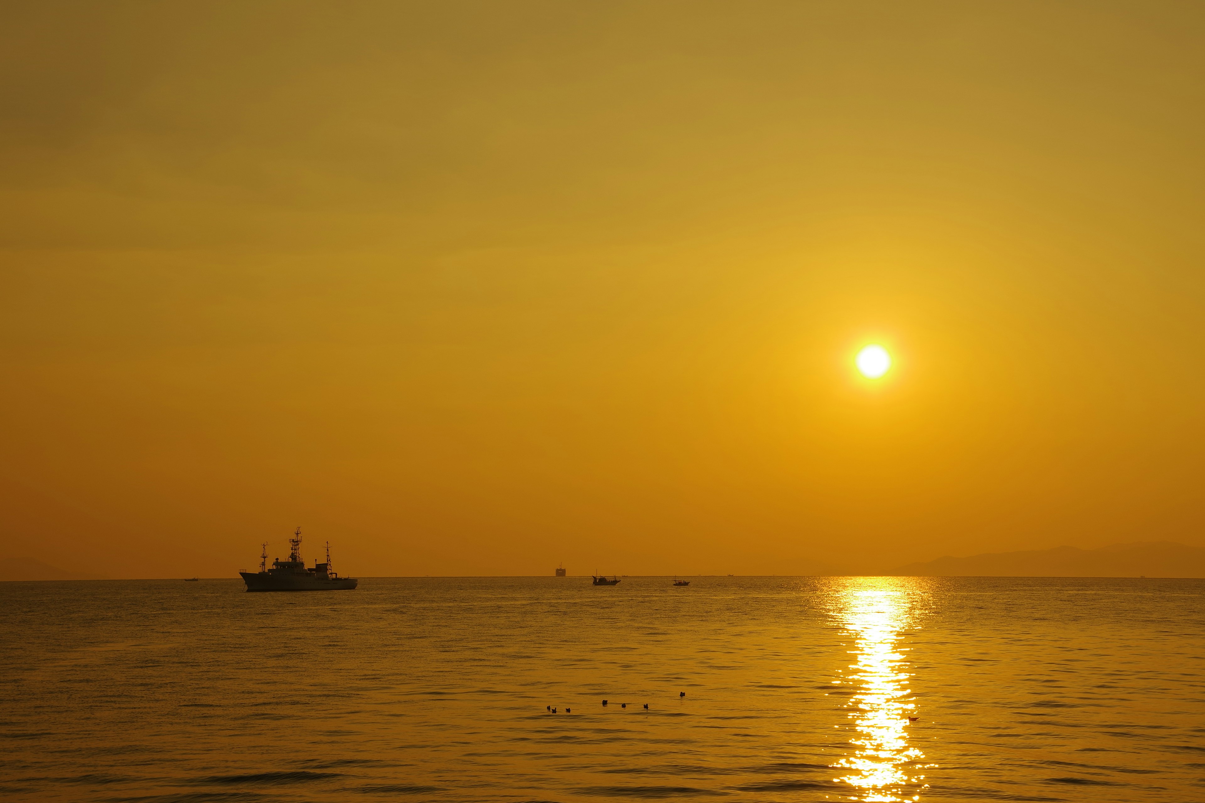 Pemandangan indah dengan matahari terbenam oranye yang memantulkan di laut sebuah kapal terlihat di kejauhan