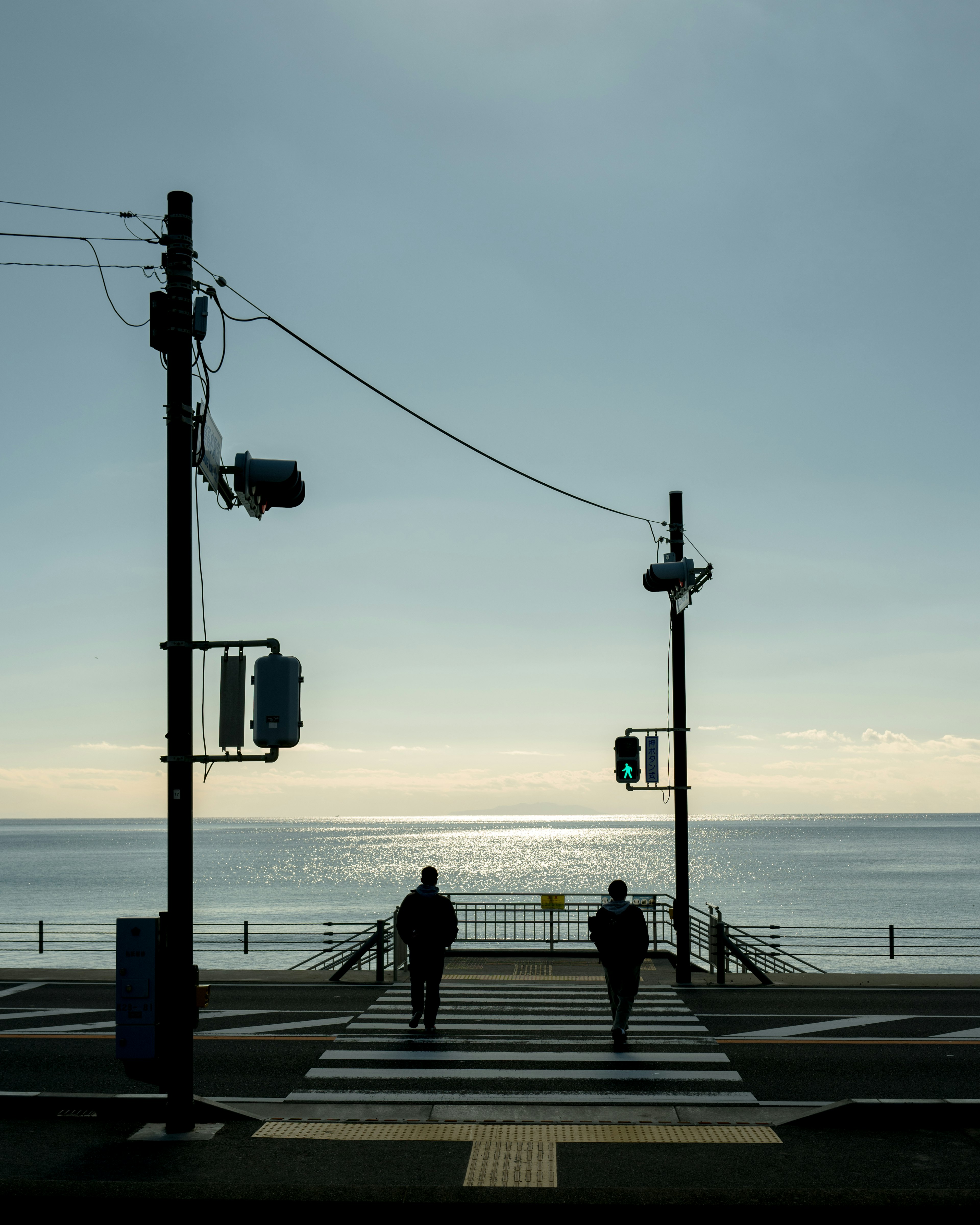 Two people crossing a pedestrian walkway with the sea in the background