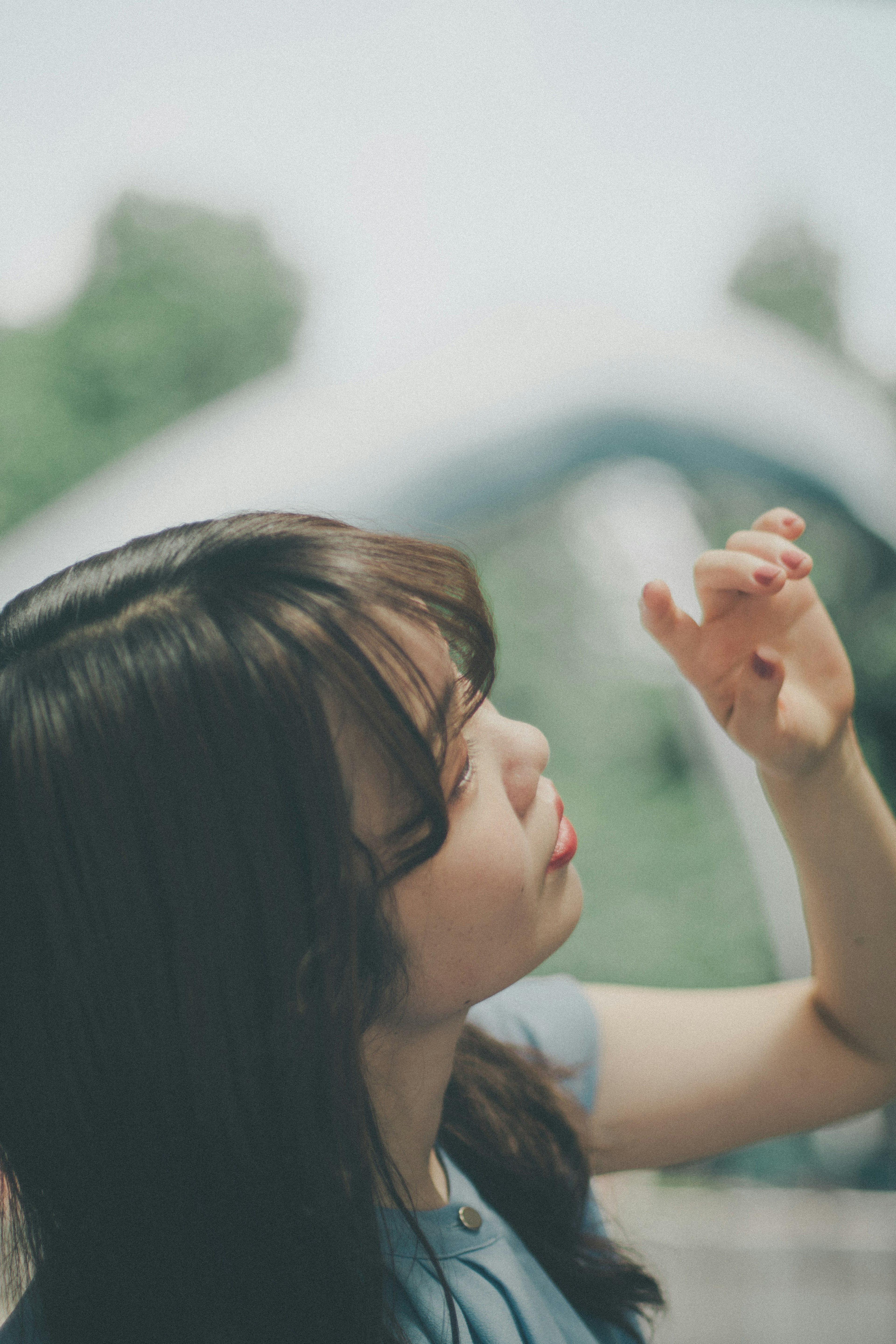 女性が手を上げて考え込んでいる姿背景に緑がある