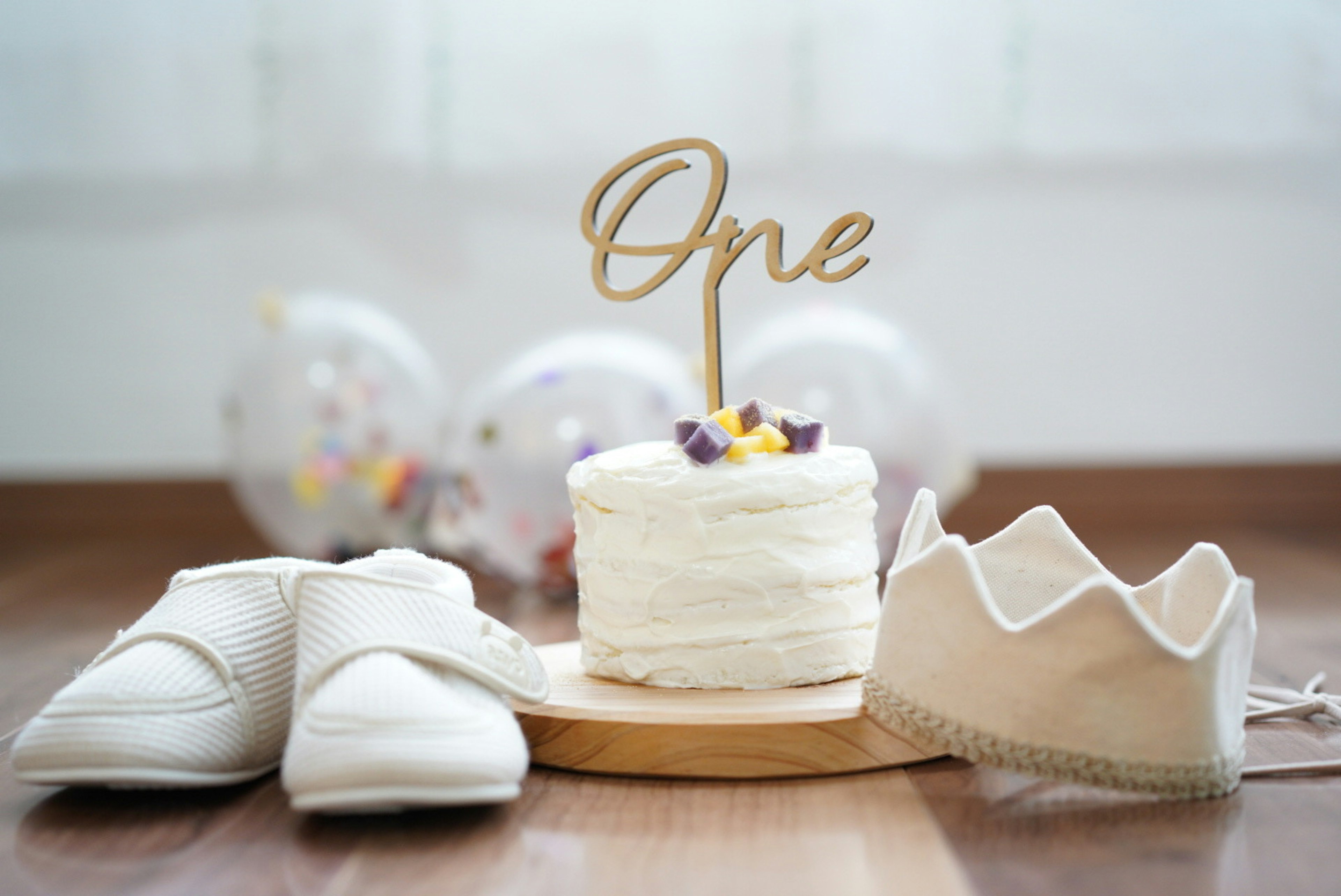 A birthday decoration featuring white shoes and a cake with a wooden 'One' topper