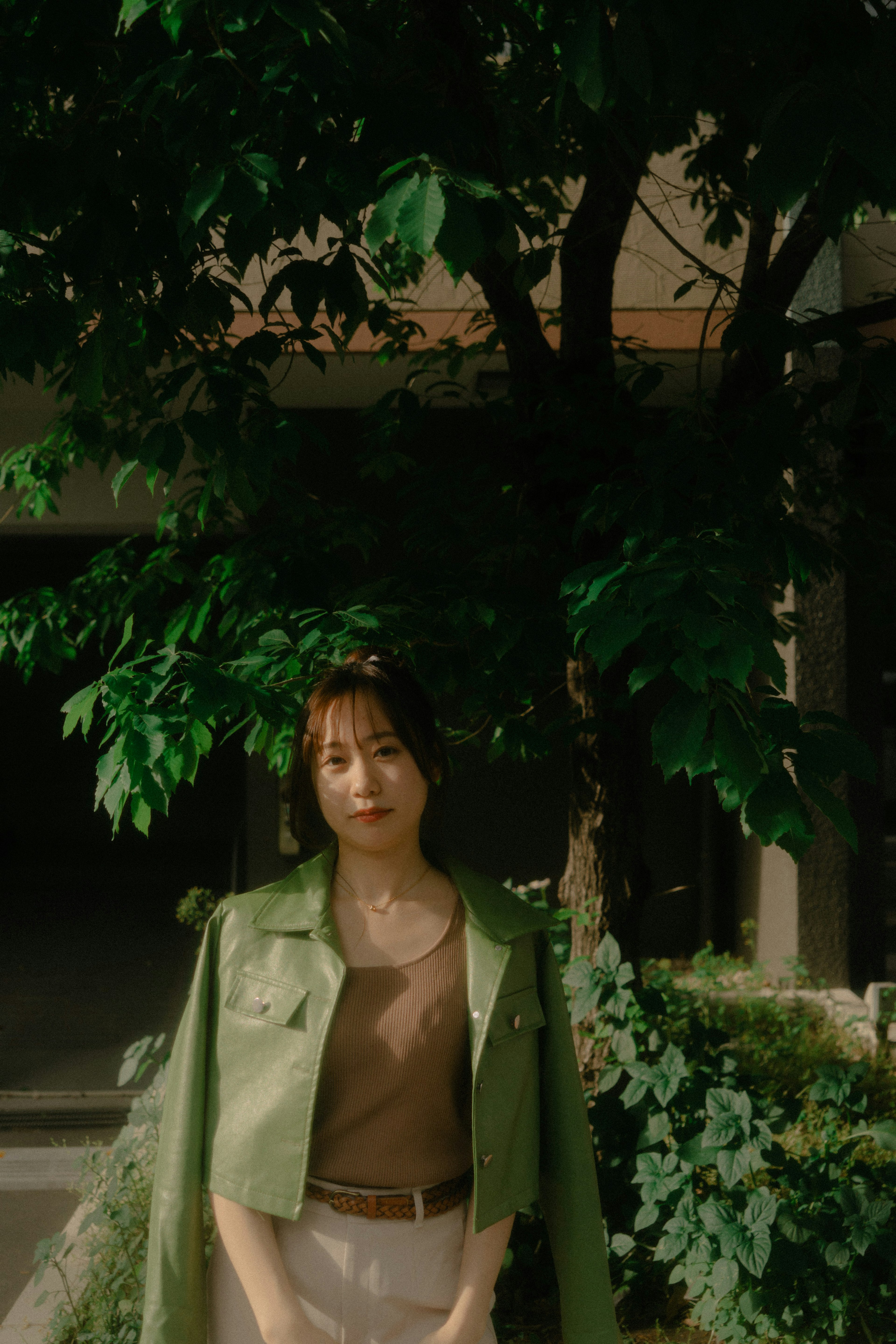 A woman wearing a green jacket stands in front of a tree