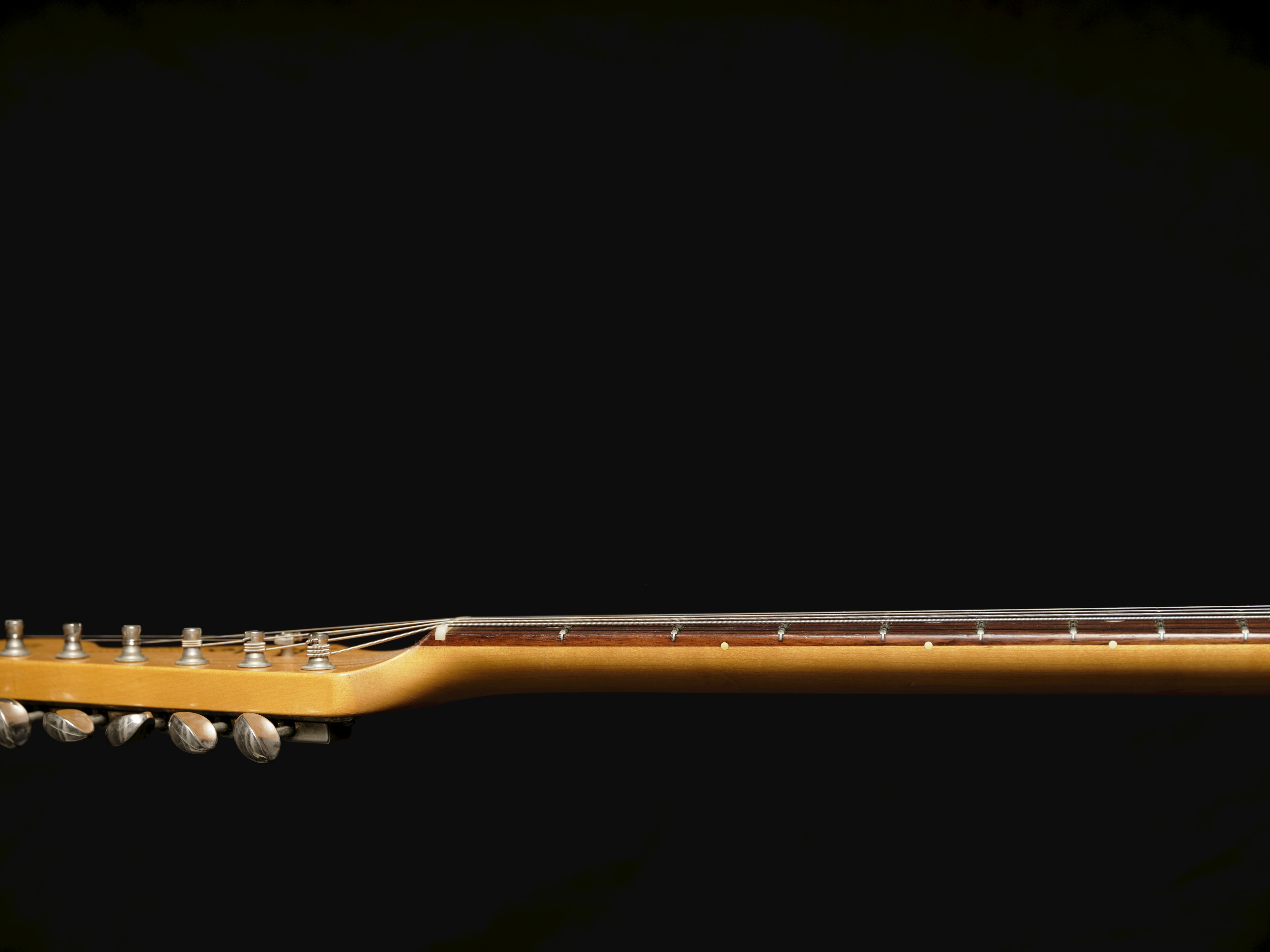 Acoustic guitar neck positioned horizontally against a black background