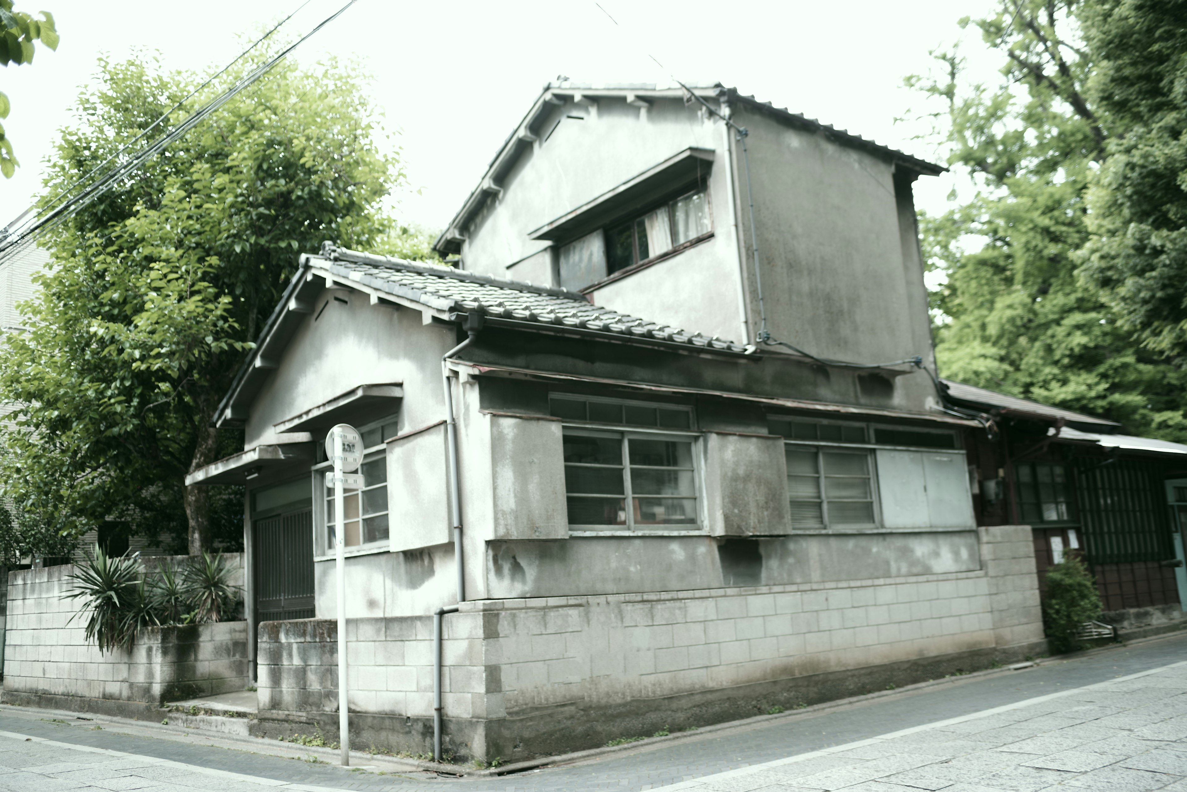 Außenansicht eines alten japanischen Hauses umgeben von grünen Bäumen und Betonwänden