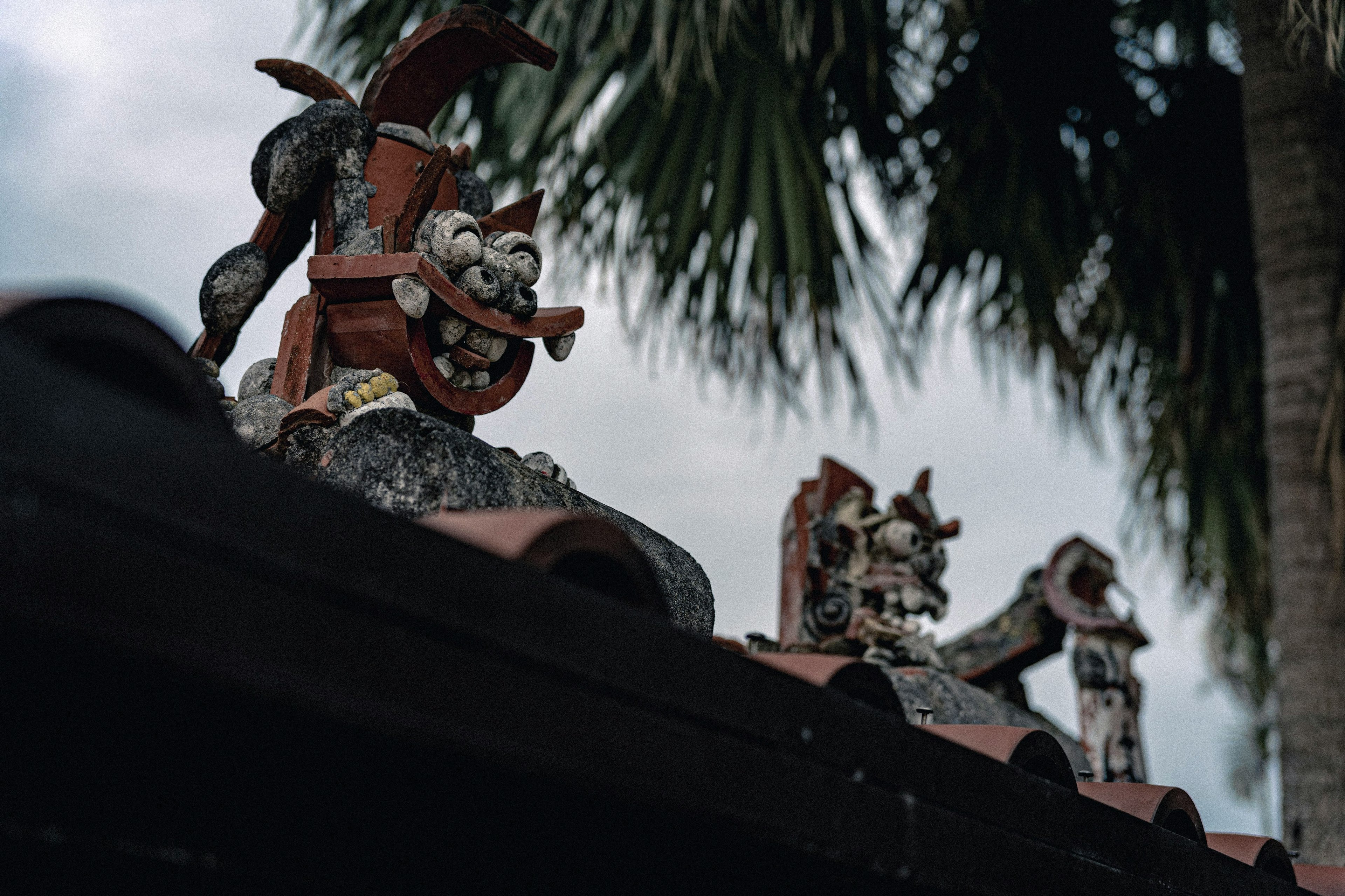 Patung tradisional di atap dengan pohon palem di latar belakang