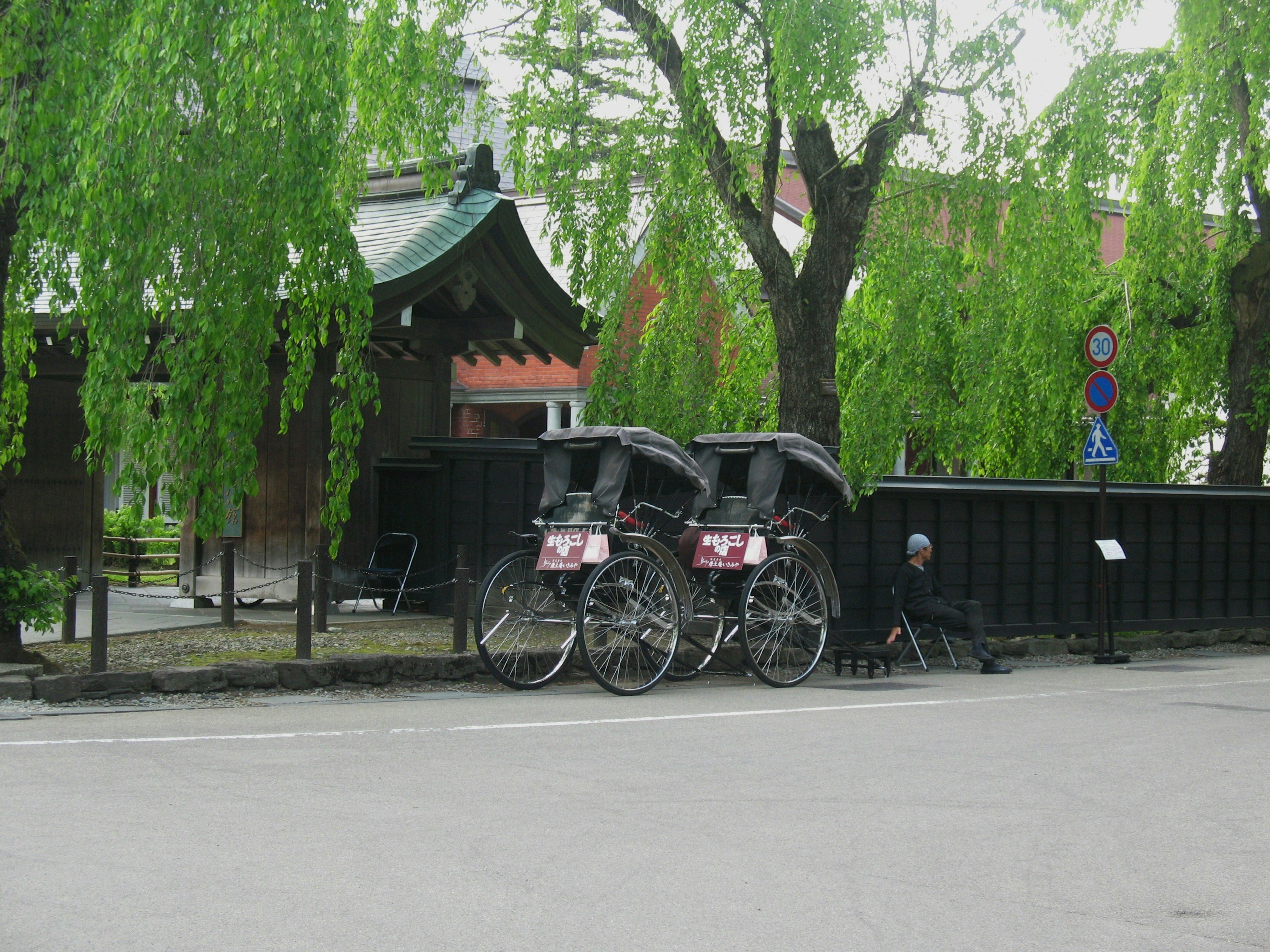 Rickshaws parked in front of traditional Japanese architecture surrounded by green willows