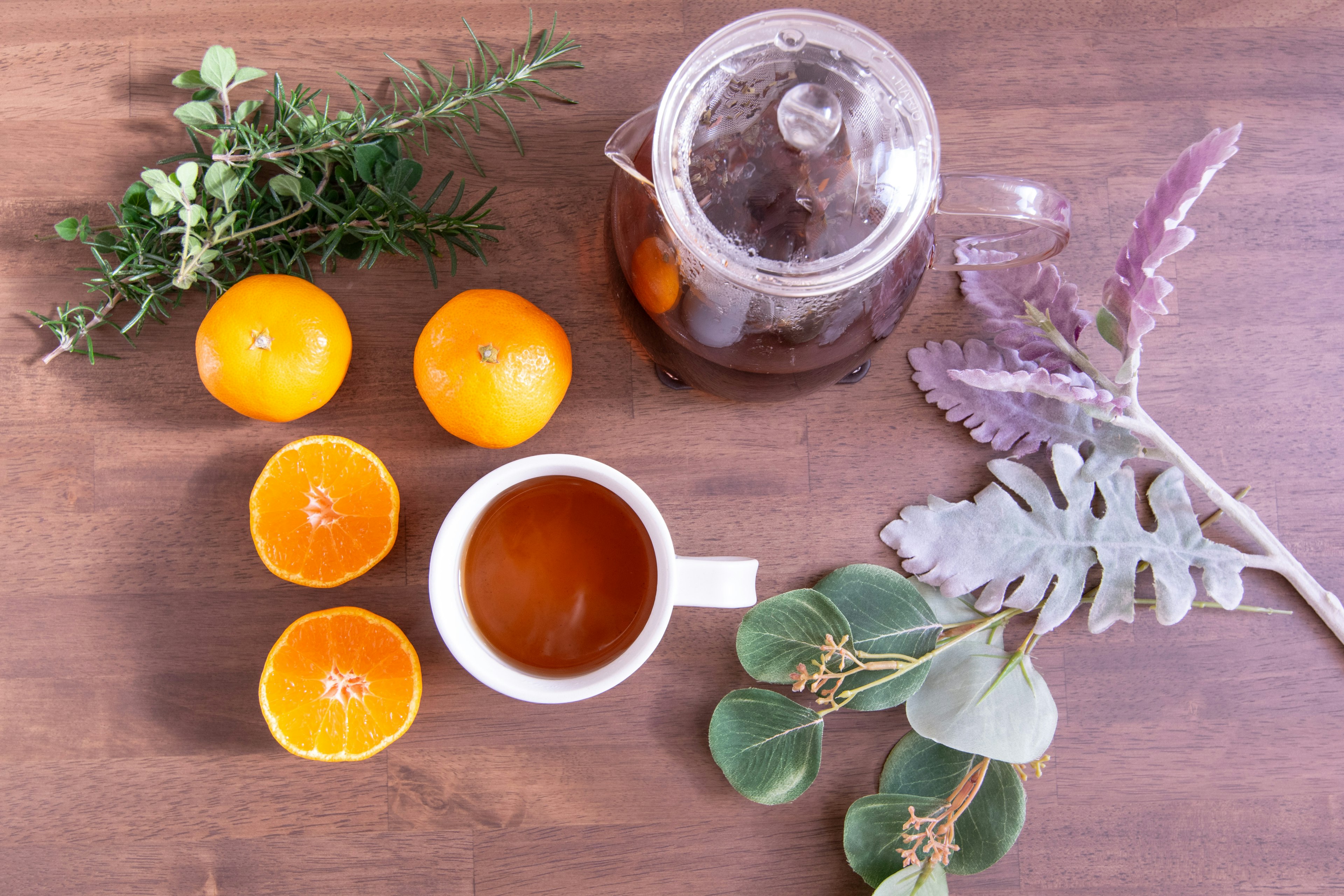 Arrangement of oranges, herbs, teapot, and cup on a wooden surface