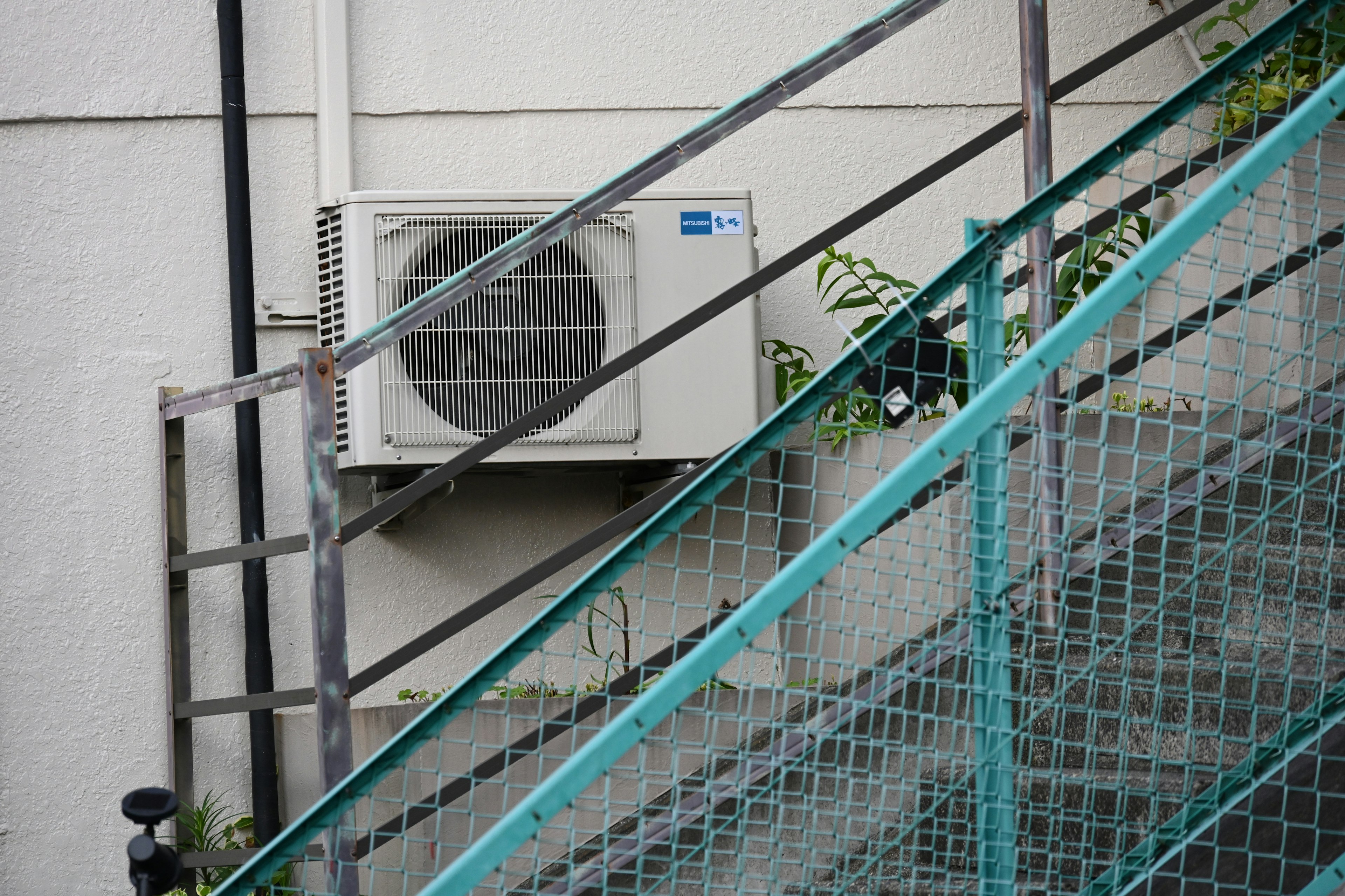 Air conditioning unit mounted on a wall beside a staircase with a mesh fence