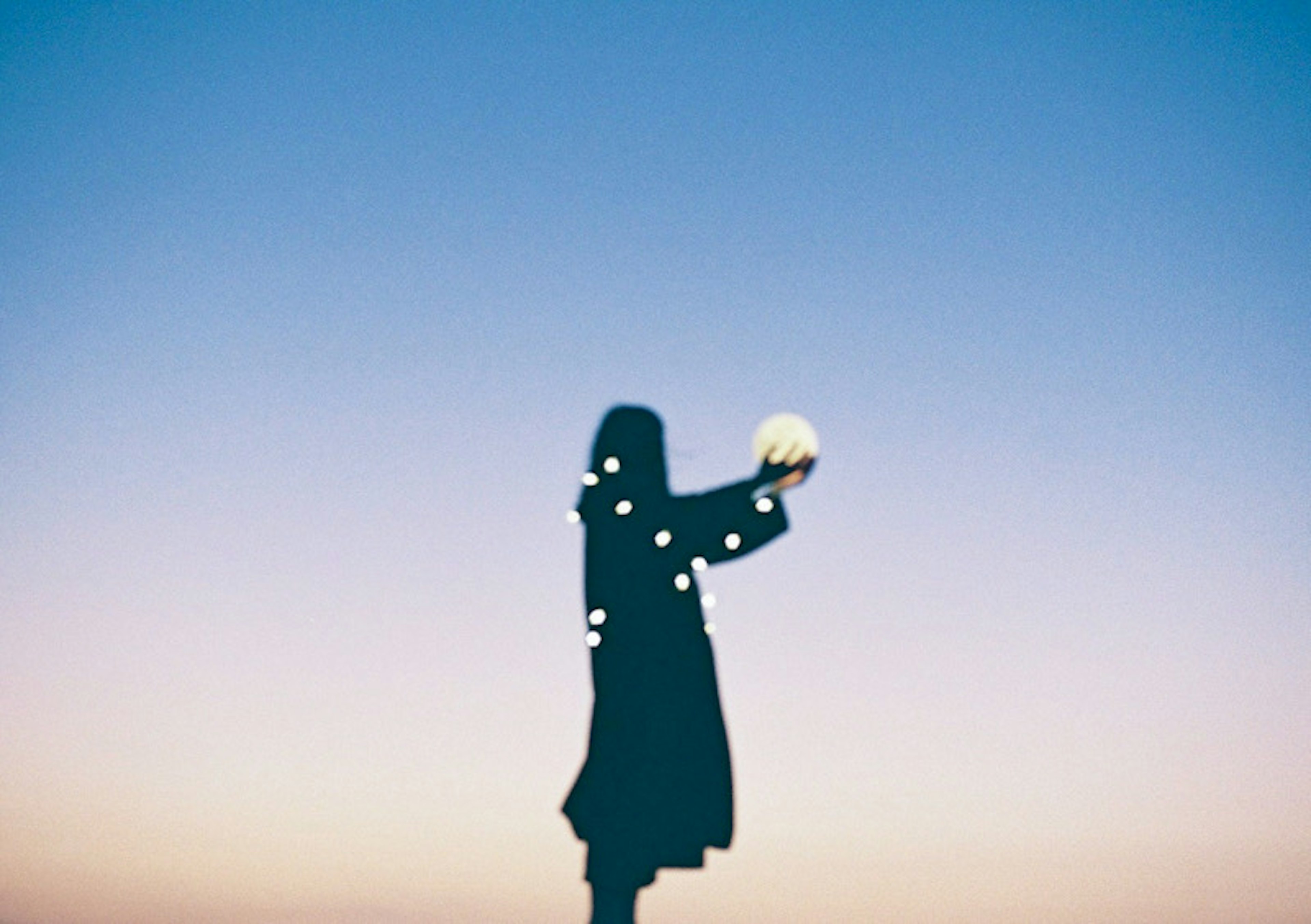 Silhouette d'une personne tenant un objet lumineux devant un ciel de coucher de soleil