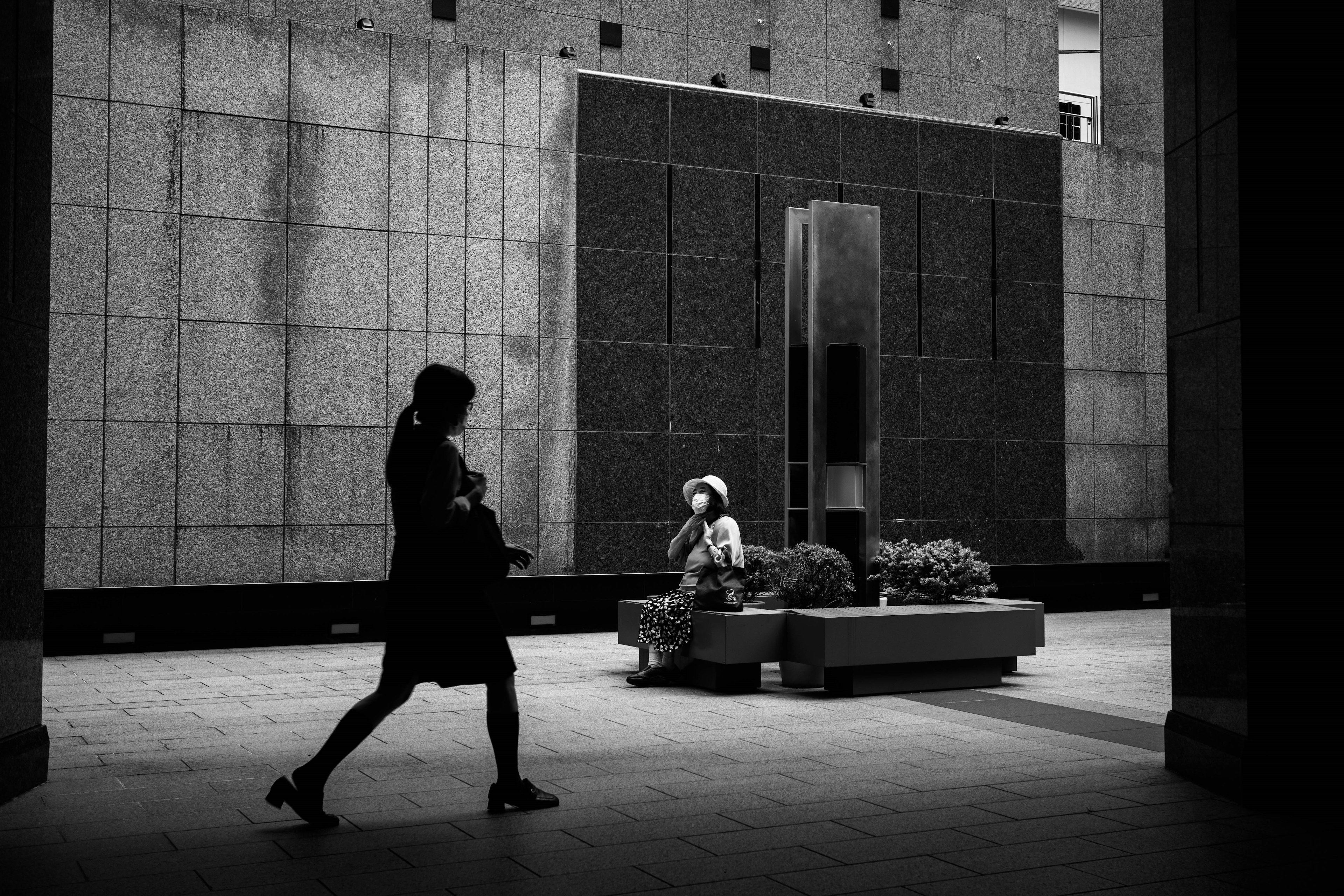 Une scène urbaine en monochrome avec une femme marchant et une autre assise avec des plantes