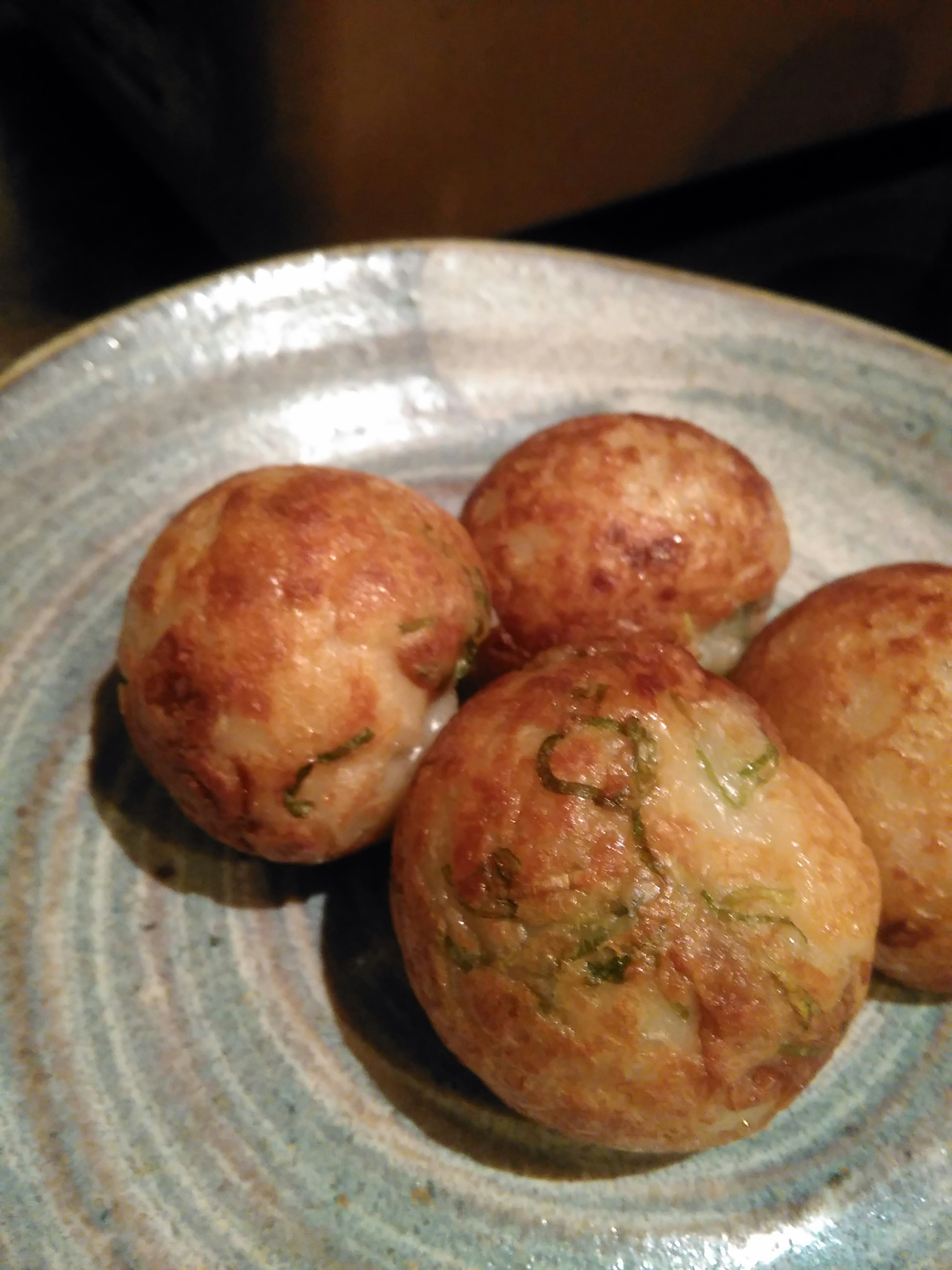 Vier goldbraune Takoyaki-Bälle auf einem blauen Teller