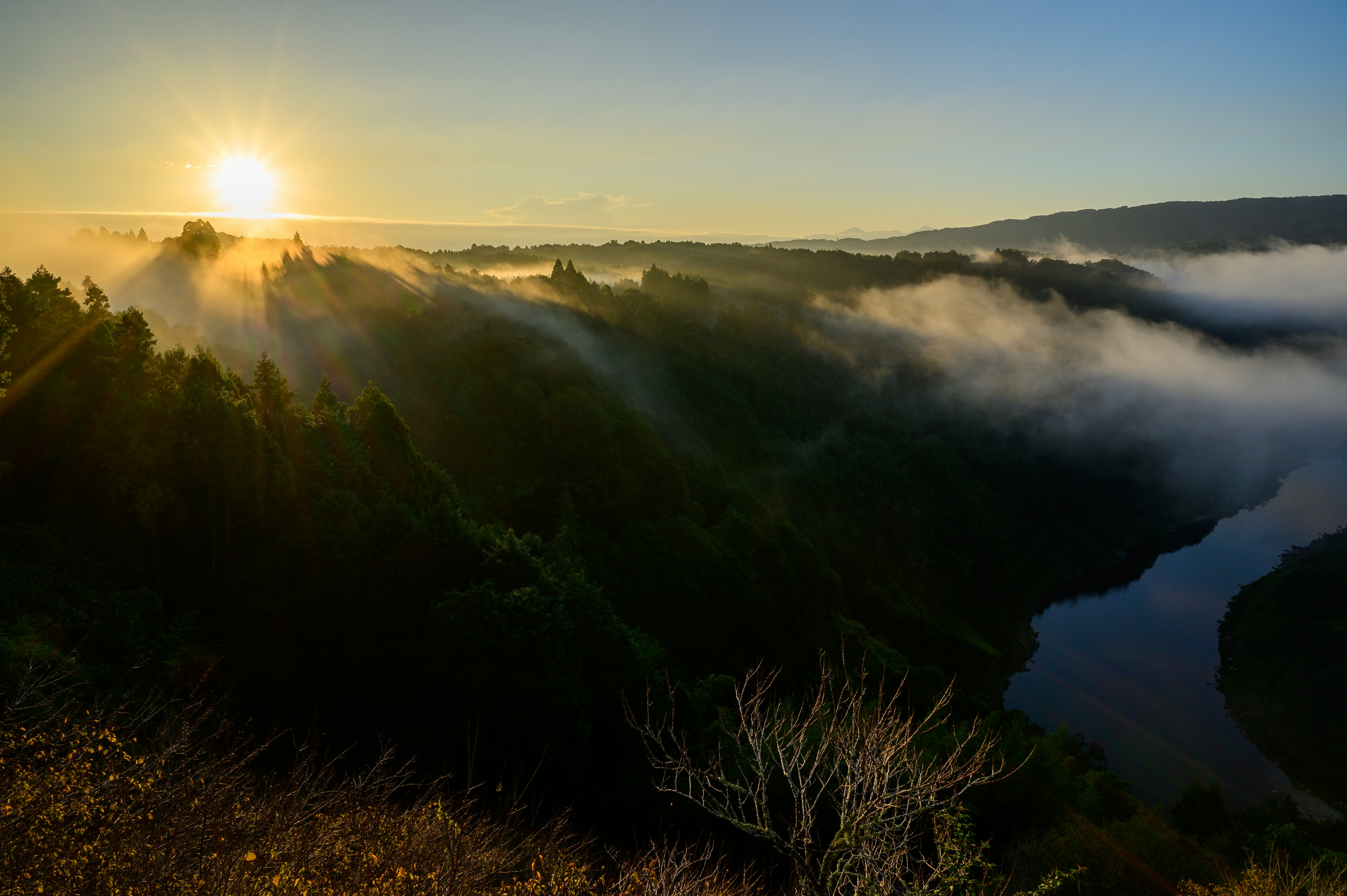 Vue panoramique de montagnes brumeuses et d'une rivière au lever du soleil illuminant le paysage