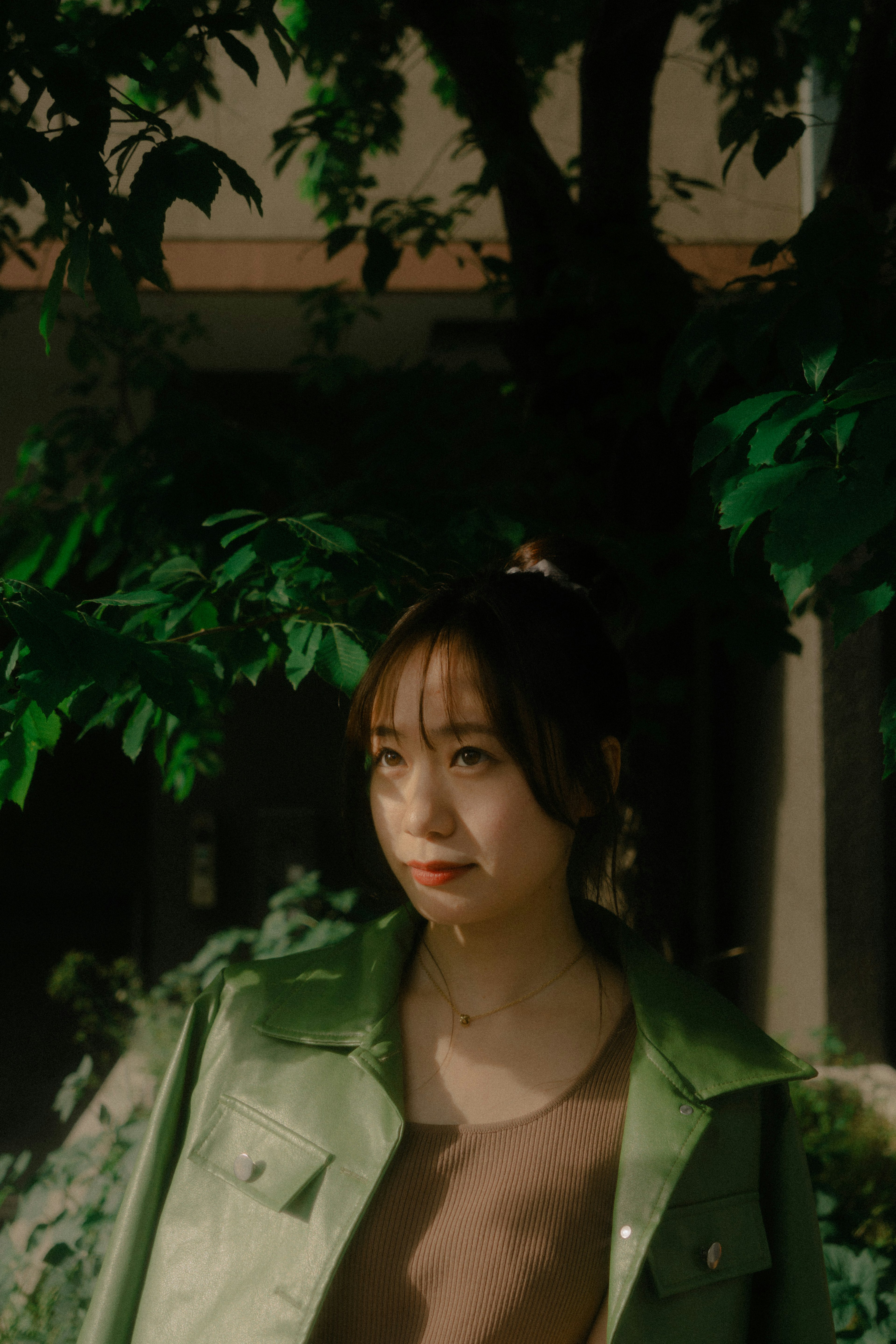 A woman in a green jacket stands in front of a tree