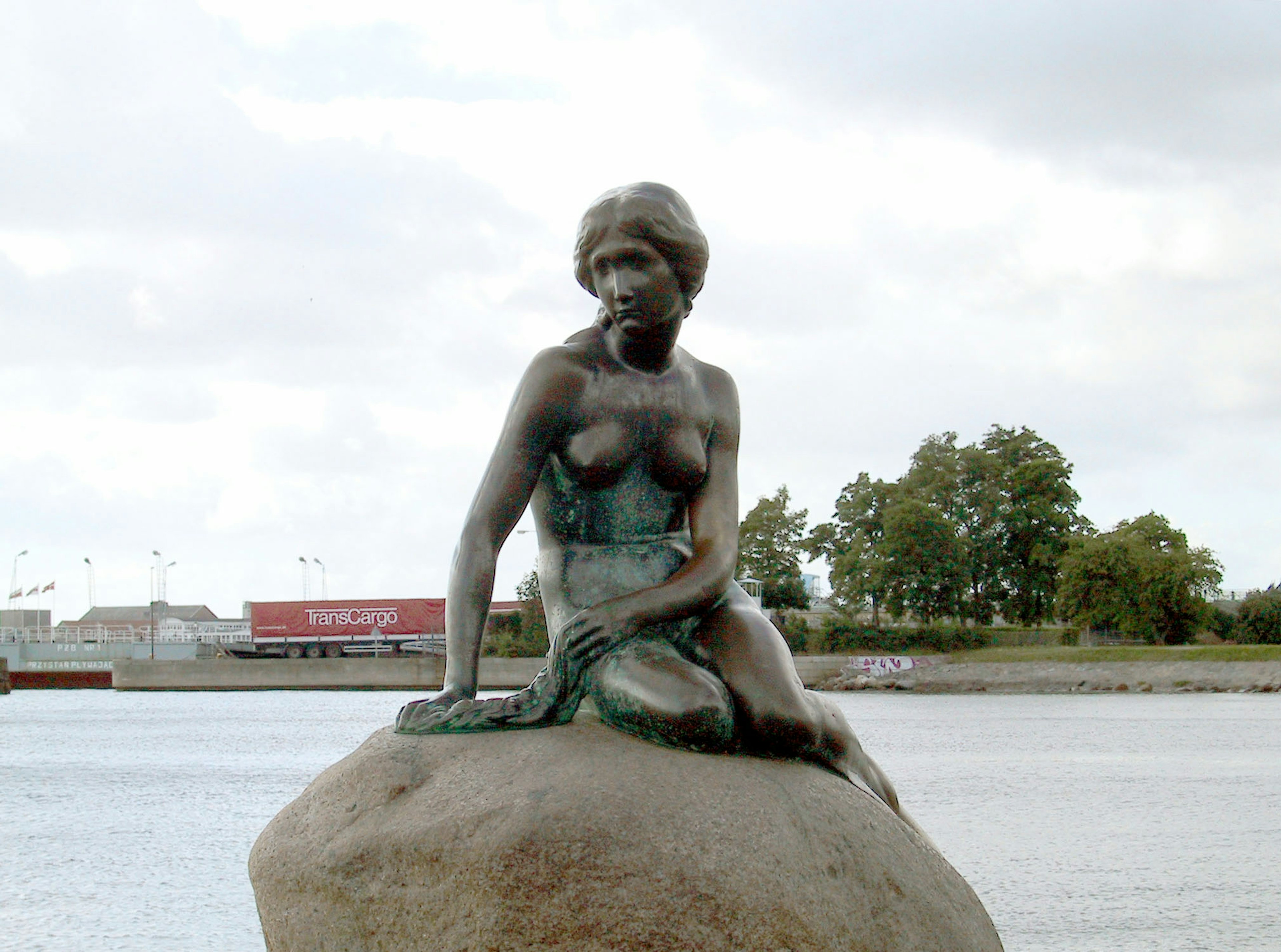 Une petite statue de sirène assise sur une roche près de l'eau