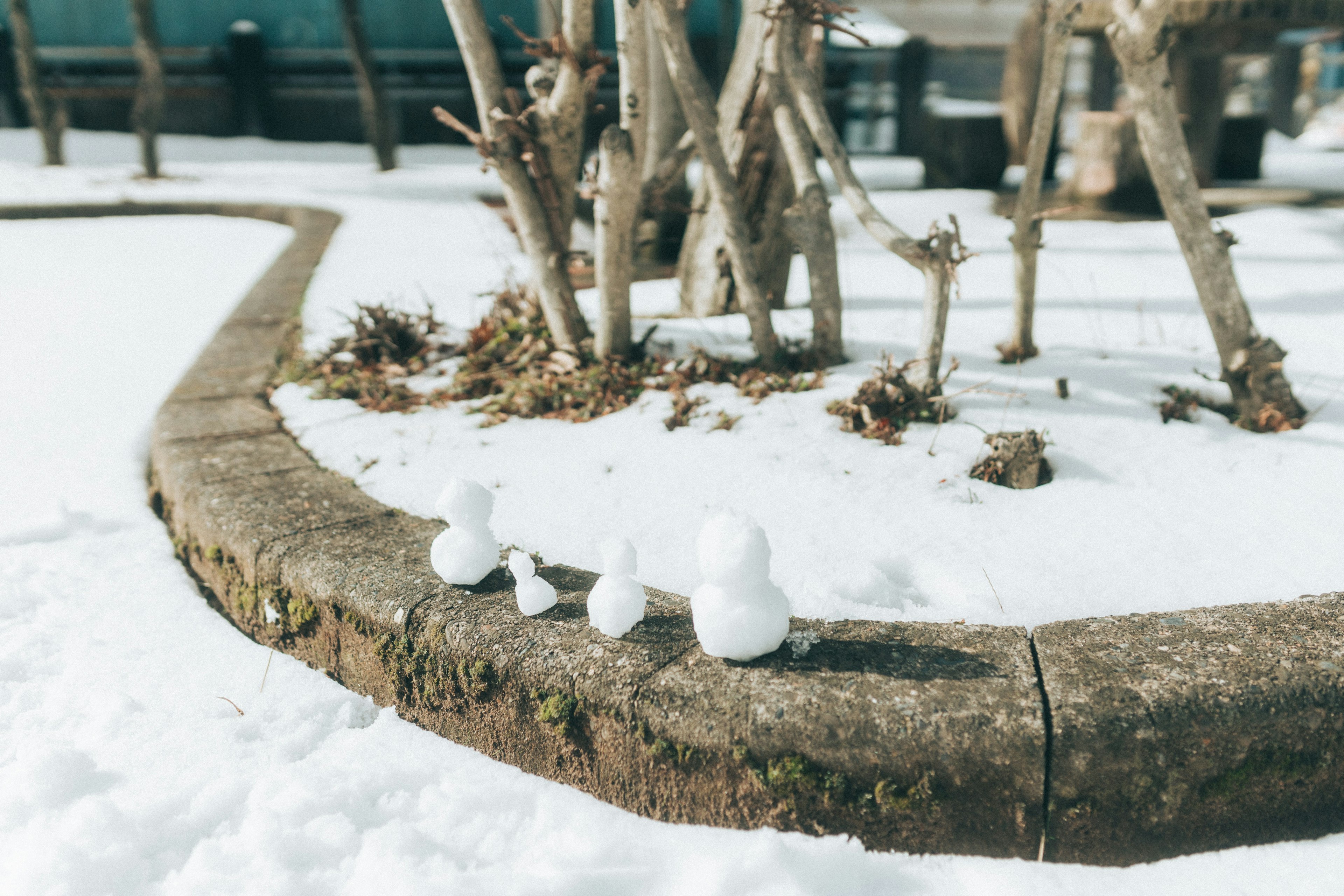 Petits bonhommes de neige alignés sur une bordure en pierre dans la neige