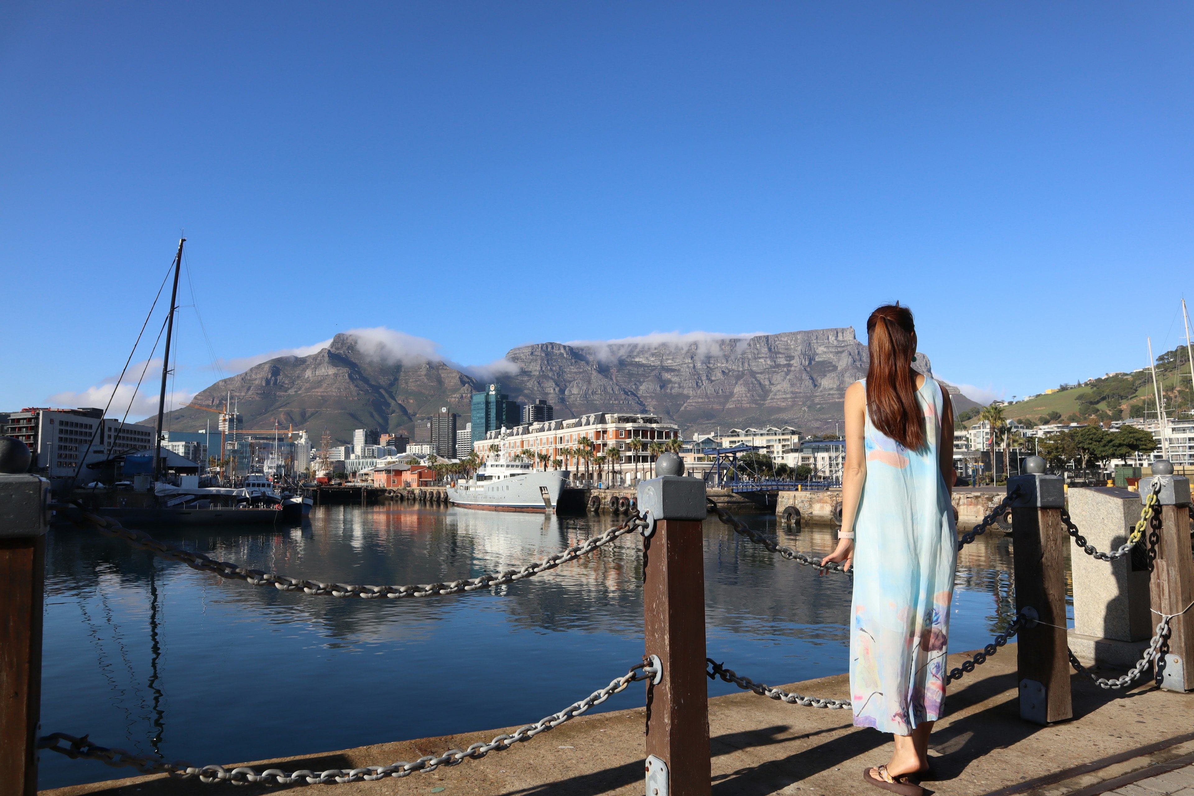 Woman walking by the harbor with mountains in the background under a clear blue sky