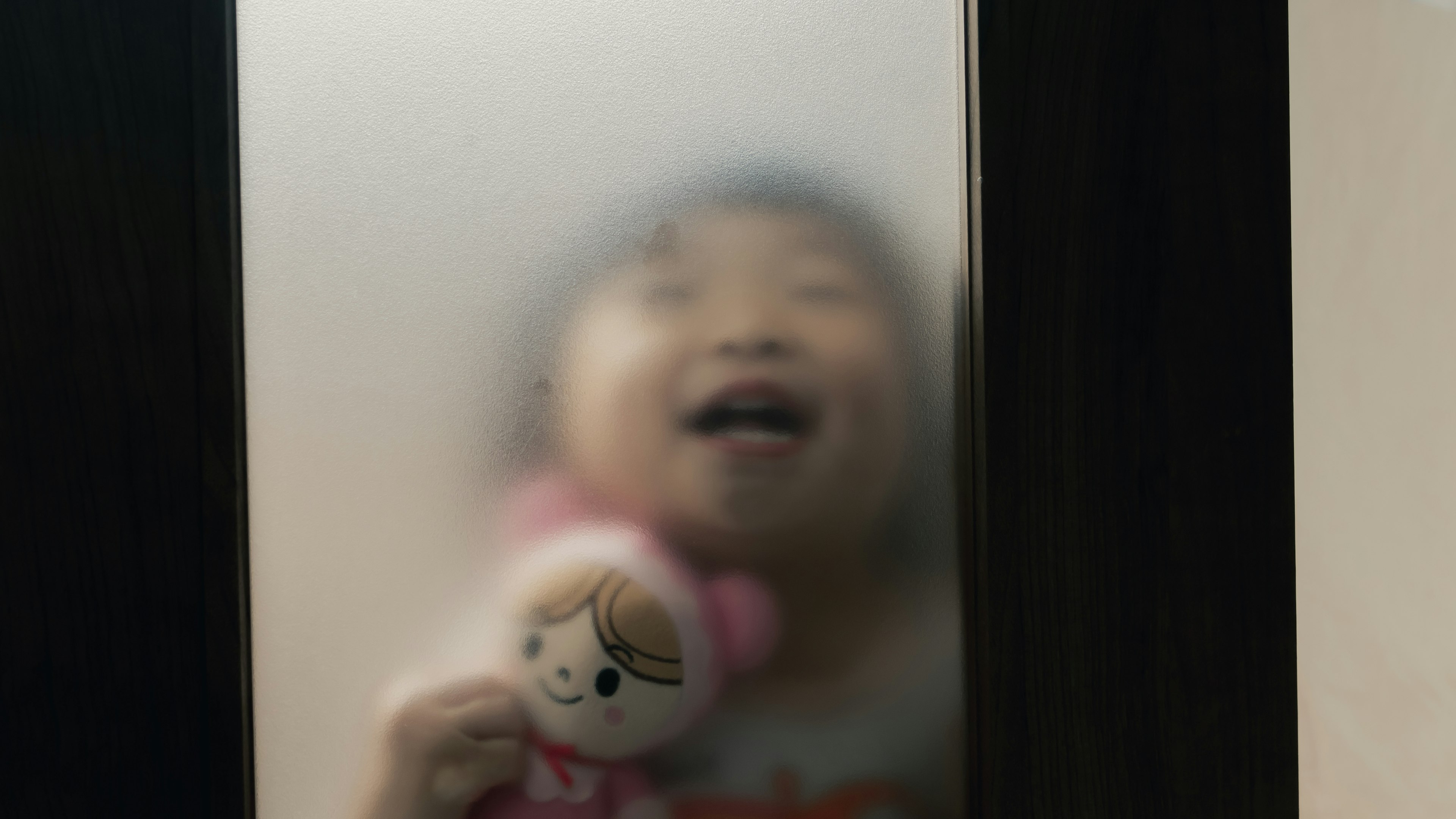 A smiling child holding a stuffed toy seen through frosted glass