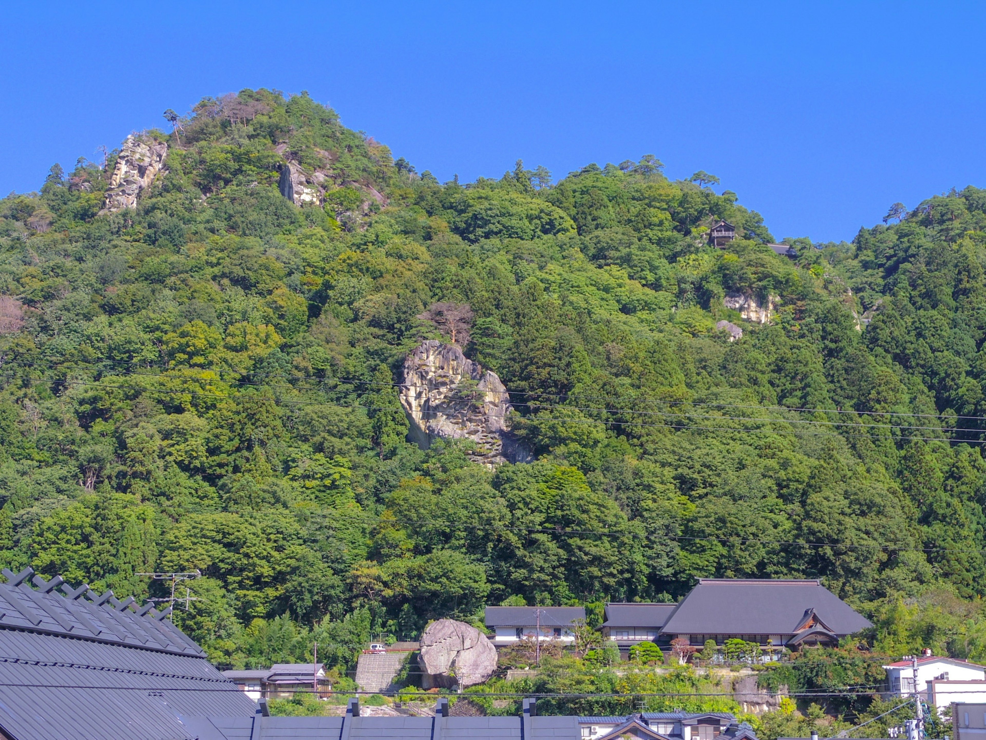 青い空と緑の山々が広がる風景 古い家屋と大きな岩が見える