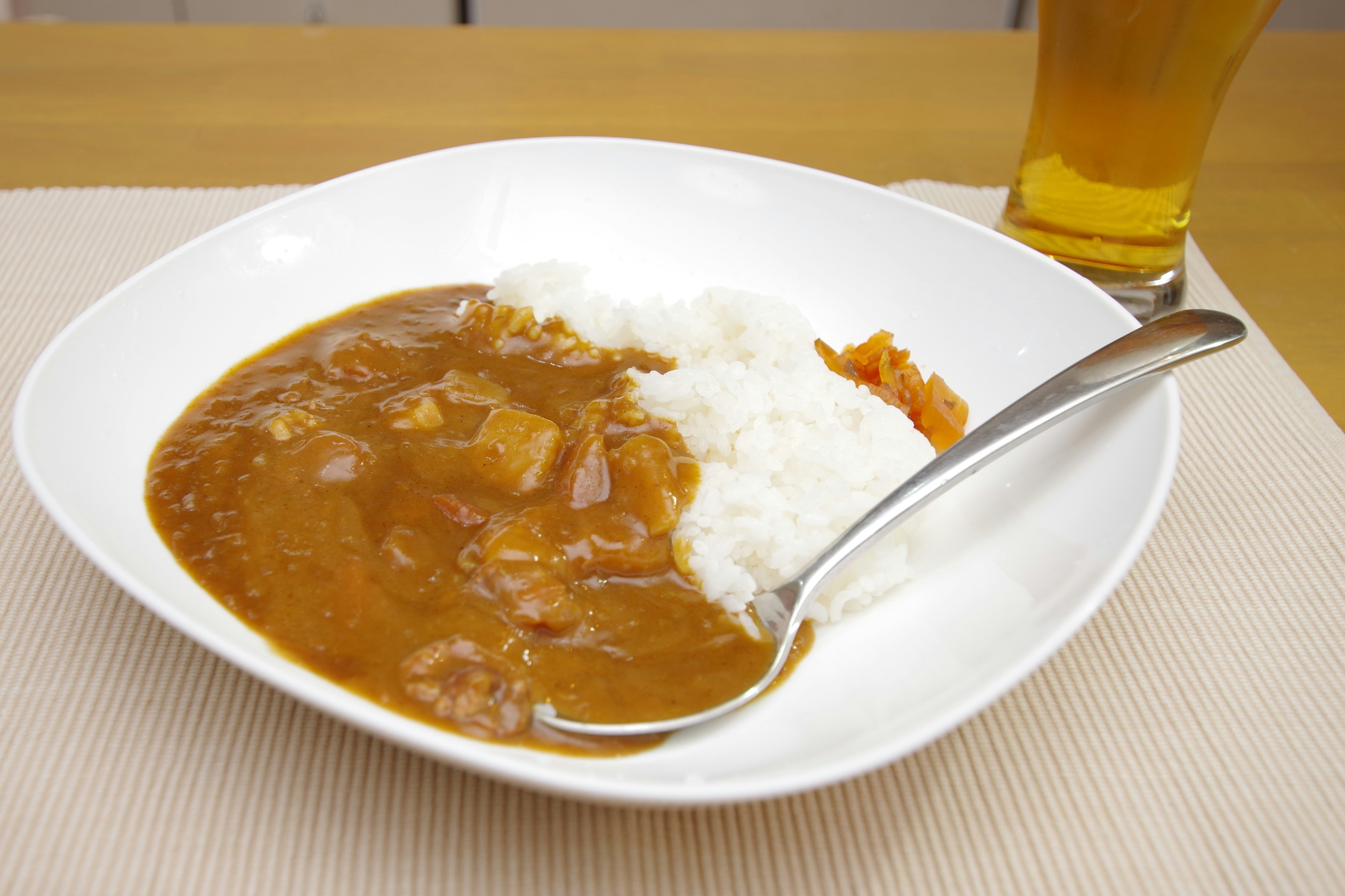 Schüssel mit Curryreis und einem Löffel sowie einem Glas Bier