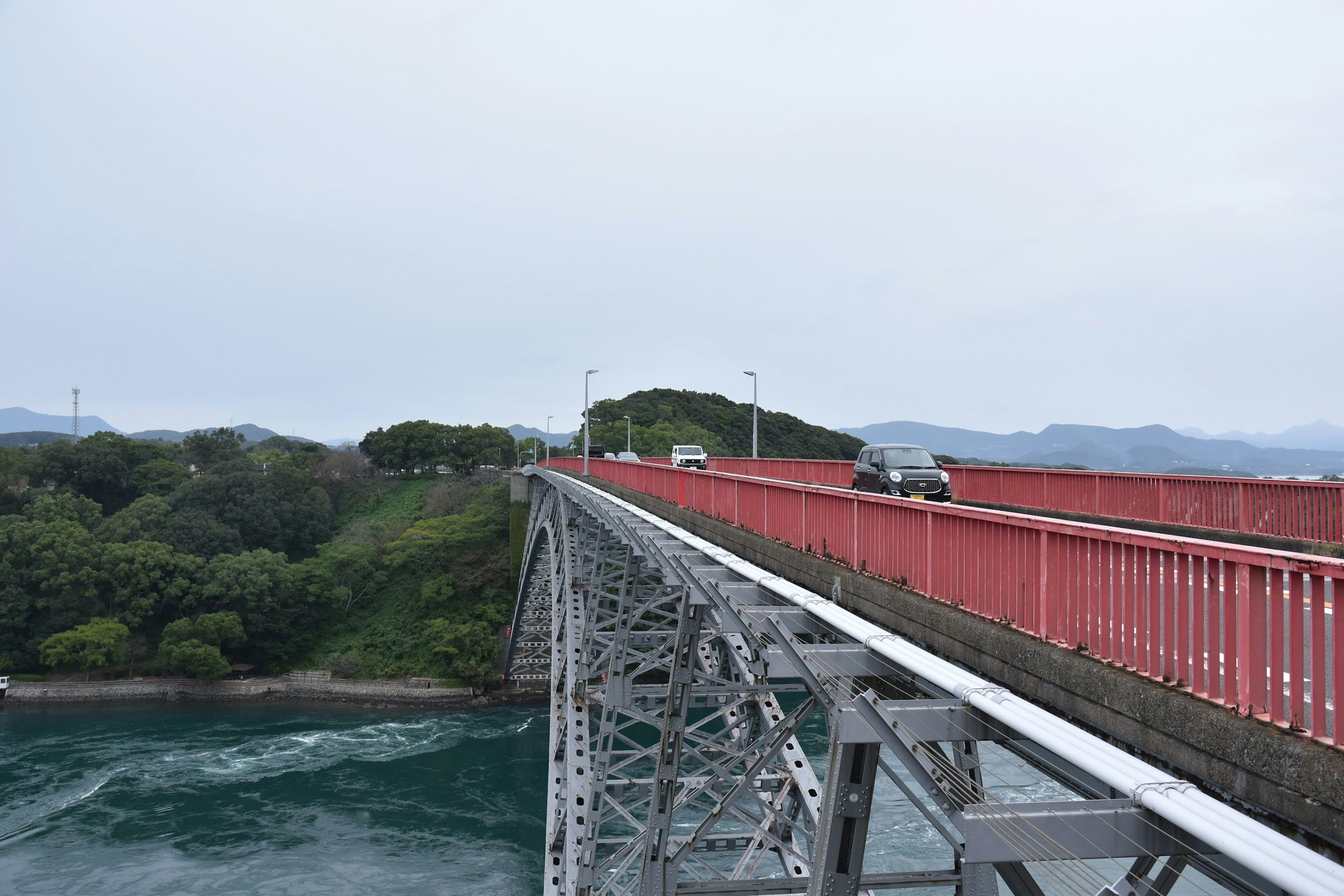 Red bridge spanning the ocean with green hills in the background