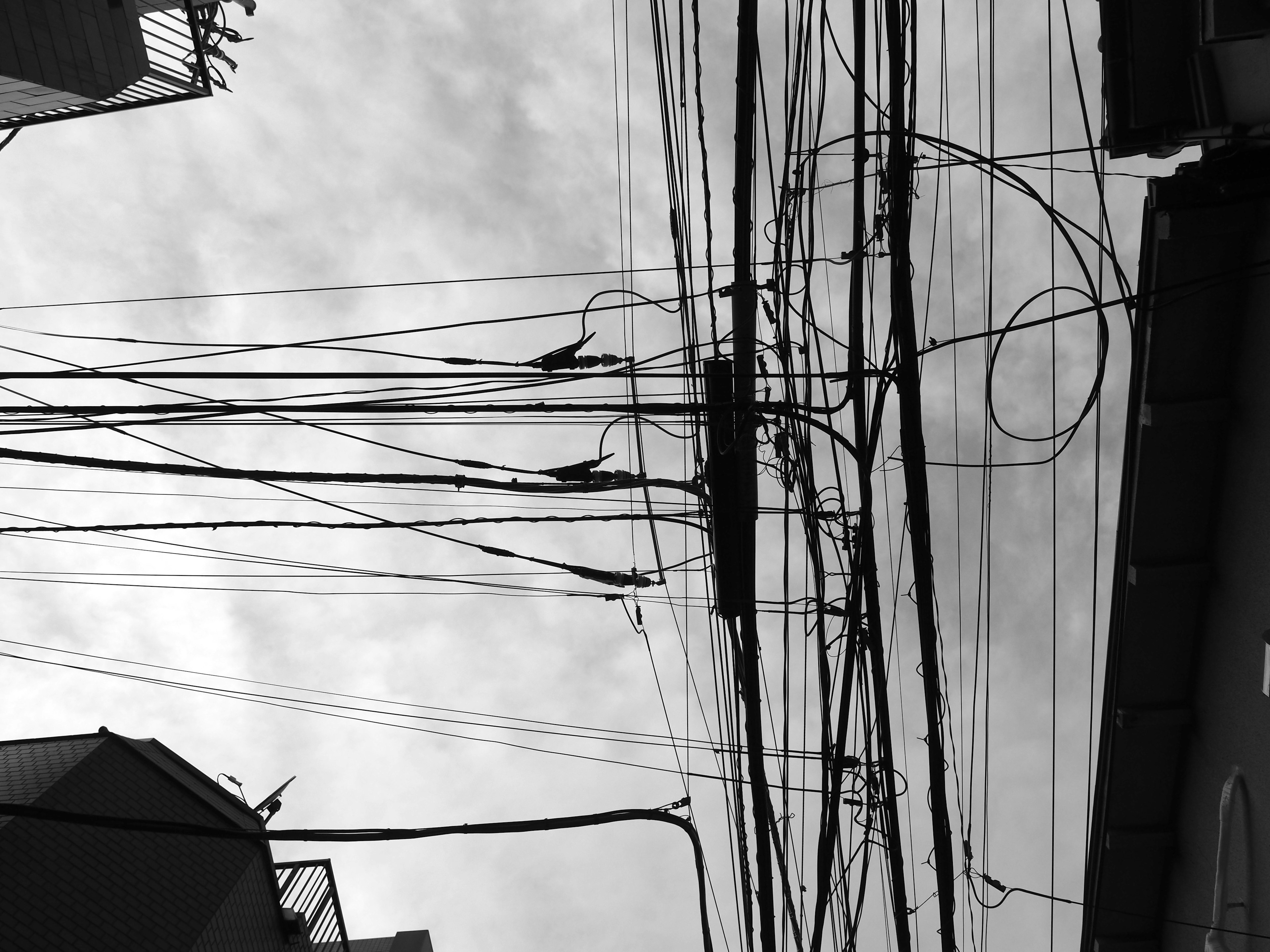 Black and white image of tangled power lines against a cloudy sky