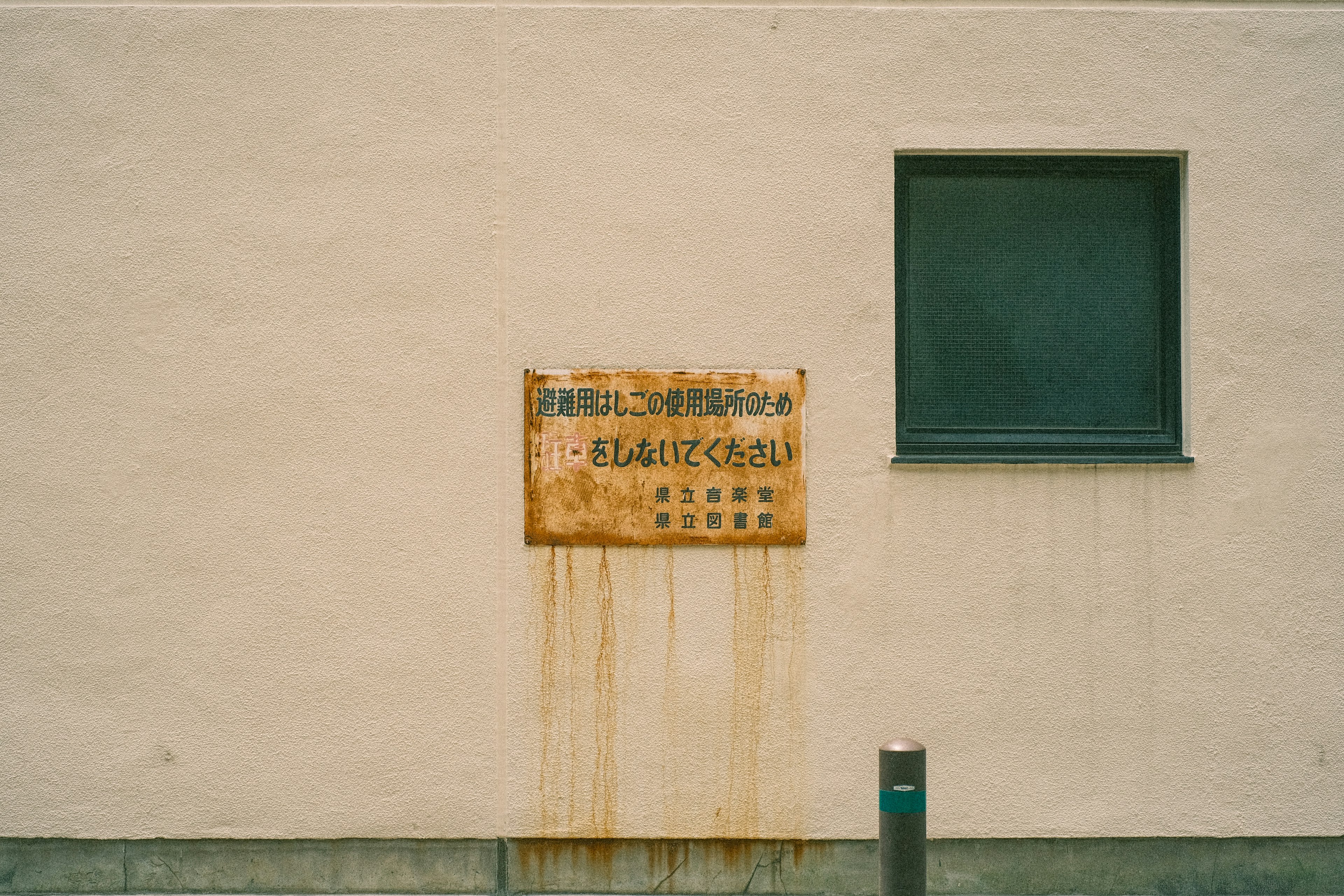 Rostiges Schild mit grünem Fenster an weißer Wand