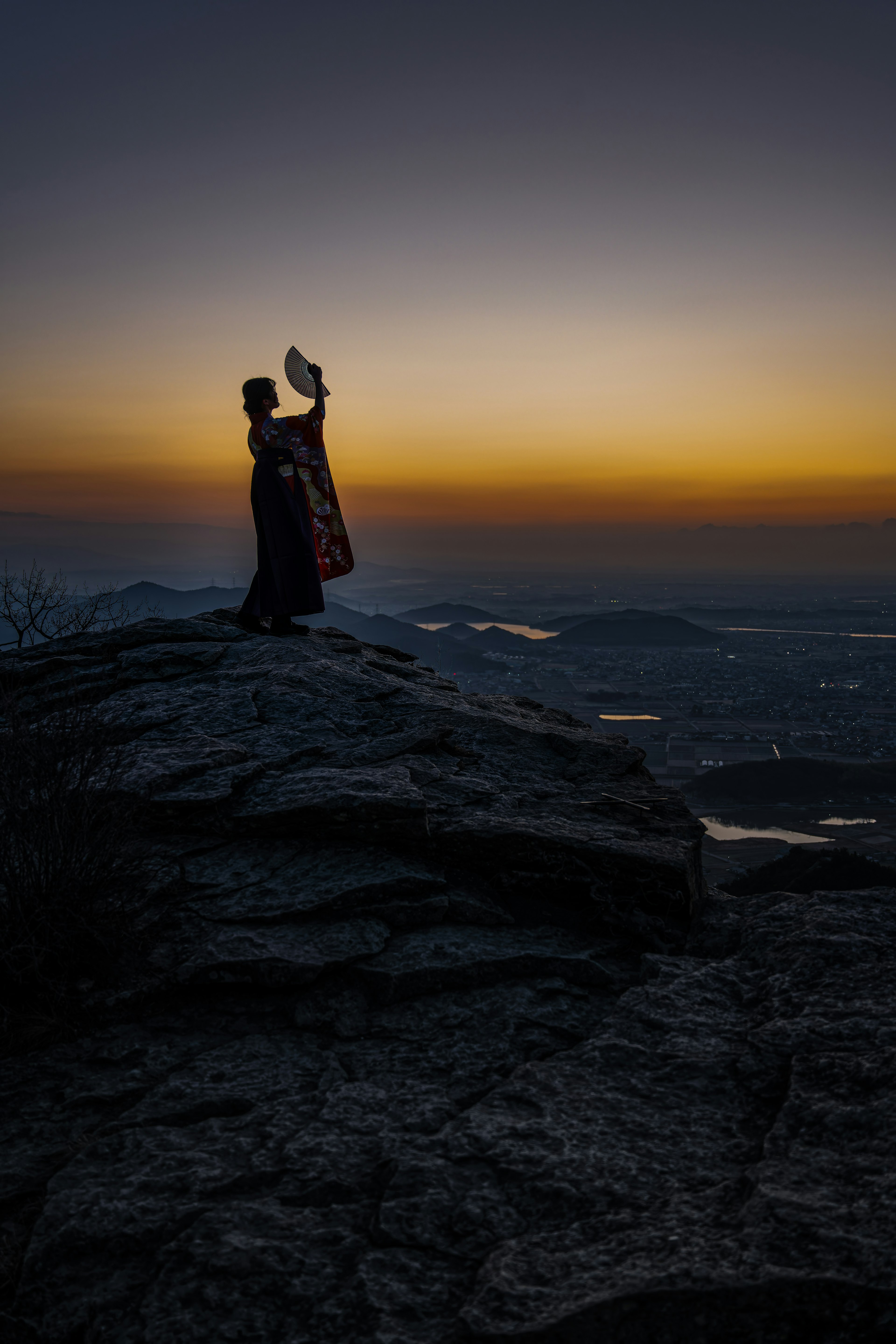 夕日を背に立つ人物が岩の上でポーズを取っている情景