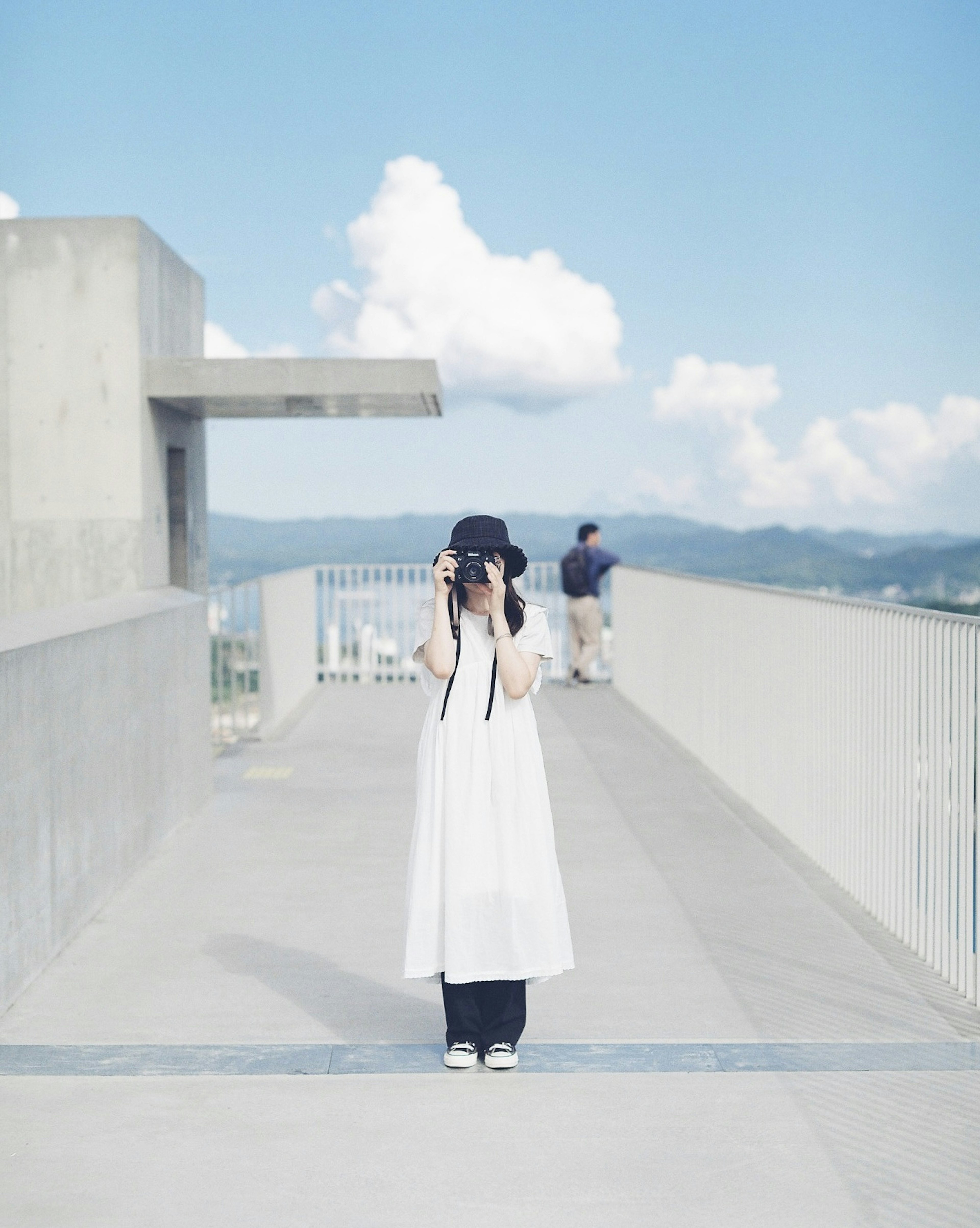 Donna in abito bianco che tiene una macchina fotografica con cielo blu e nuvole sullo sfondo